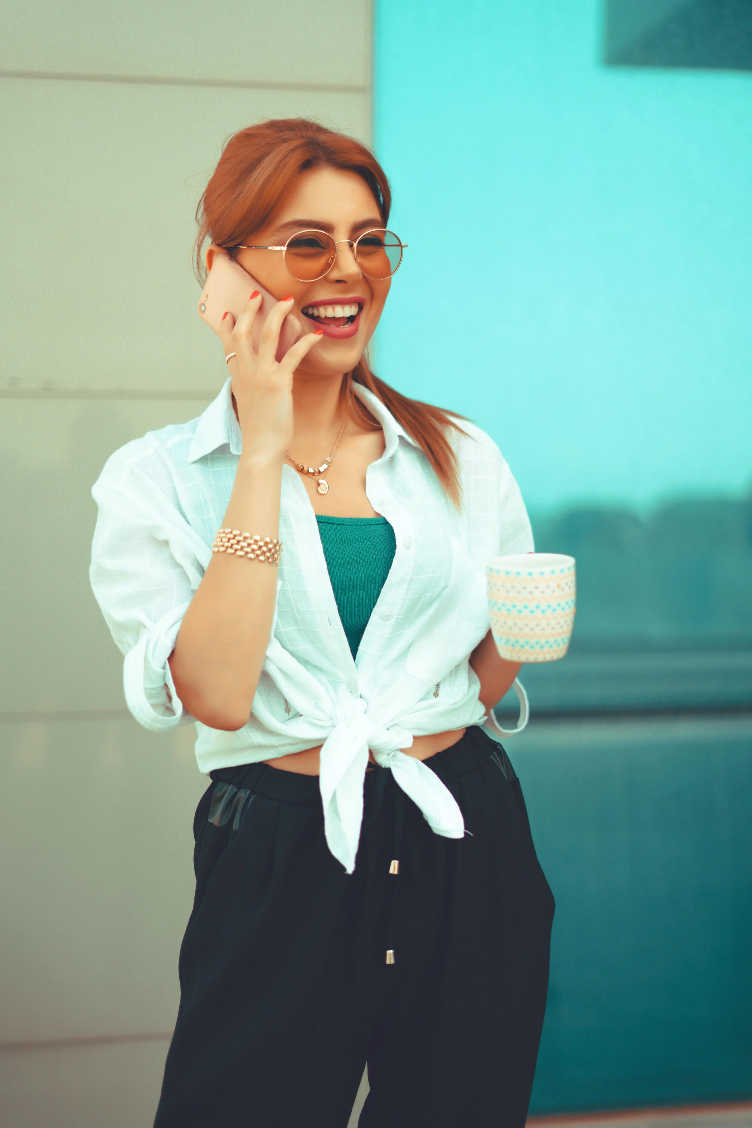 Women smiling while talking on a cell phone while holding a cup of coffee in the other hand