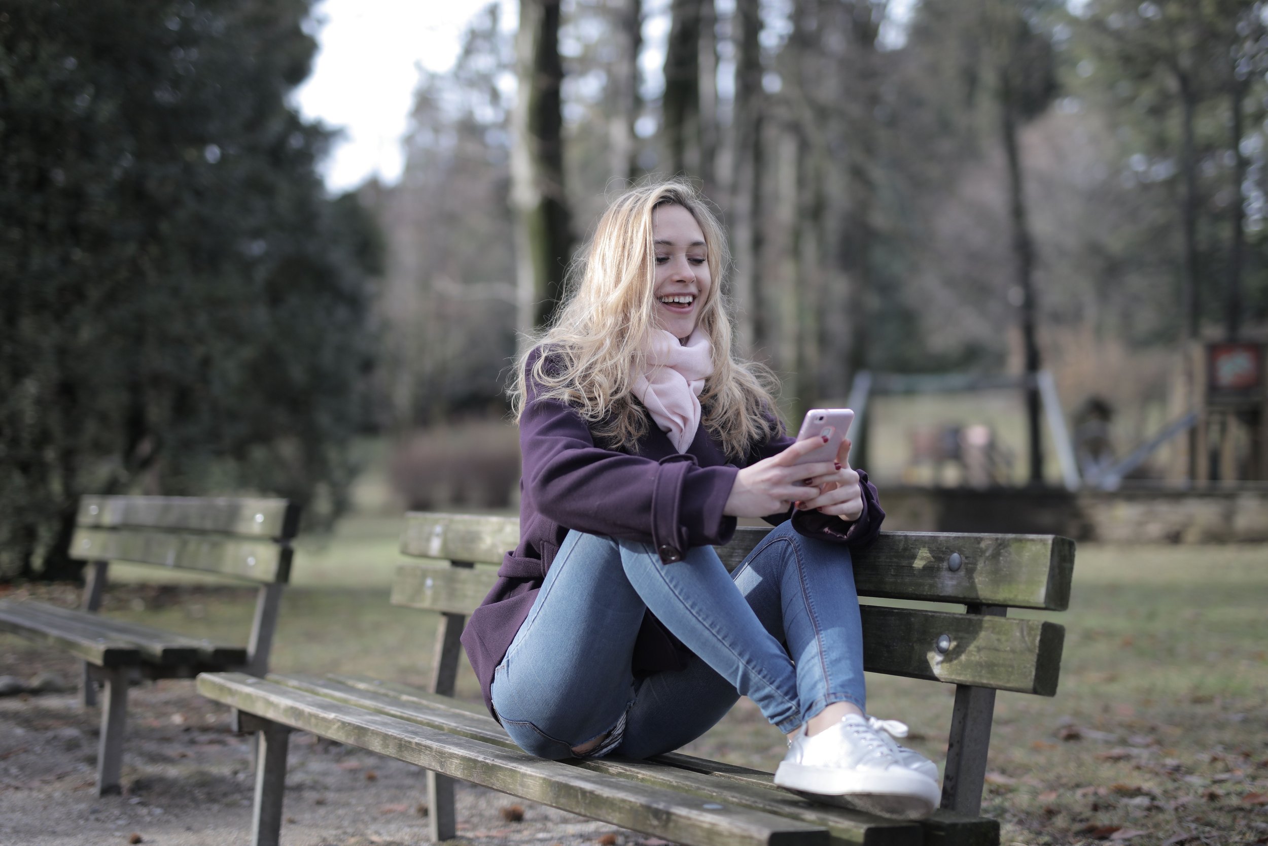 A women on a park bench smiling and looking down at her phone