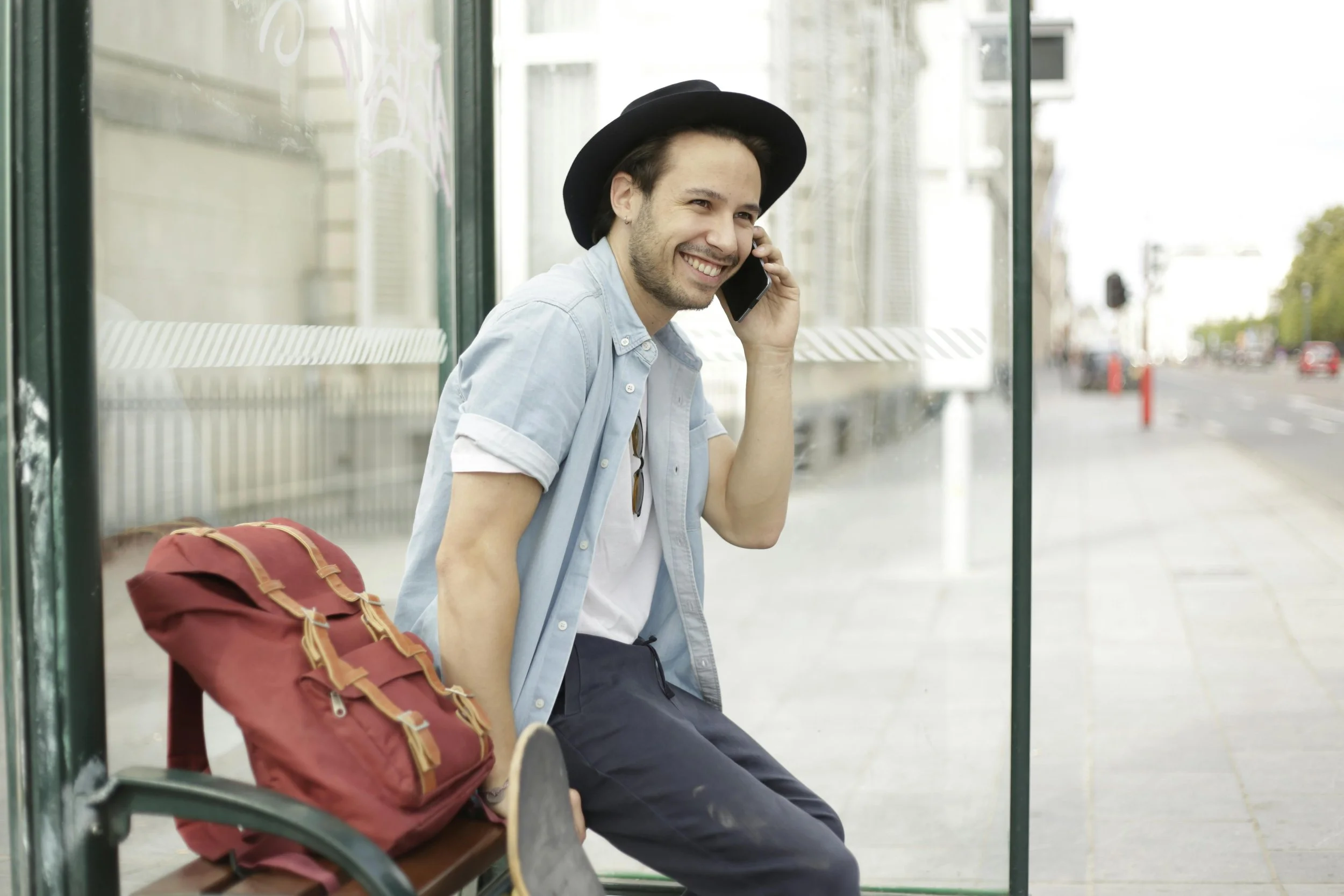 Man with a hat smiling while on his cell phone at a bus stop