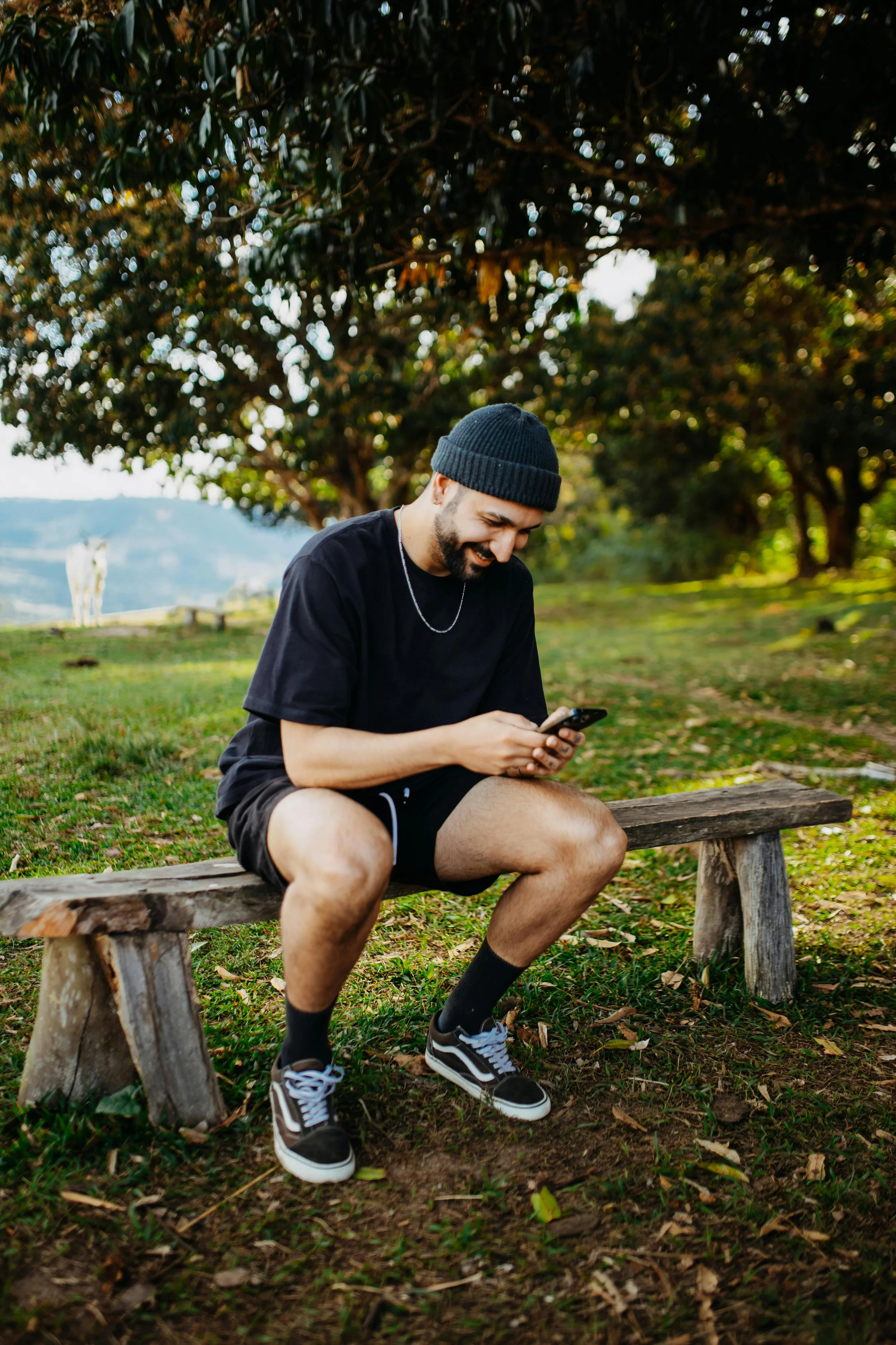 Man sitting at a park bench smiling while looking down at his smartphone