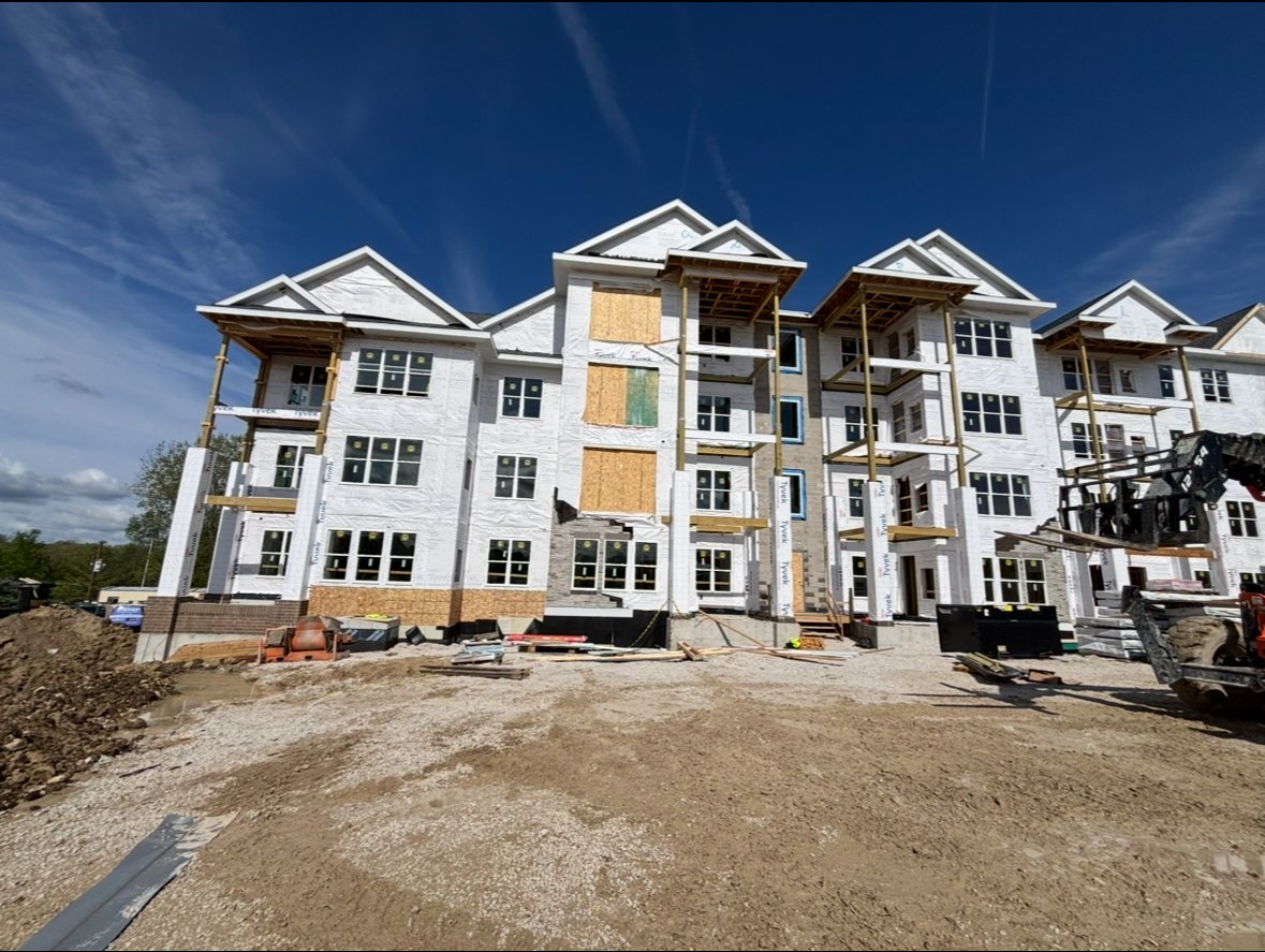 Under construction multi-story apartment building with white exterior, scaffolding, and construction equipment on site.