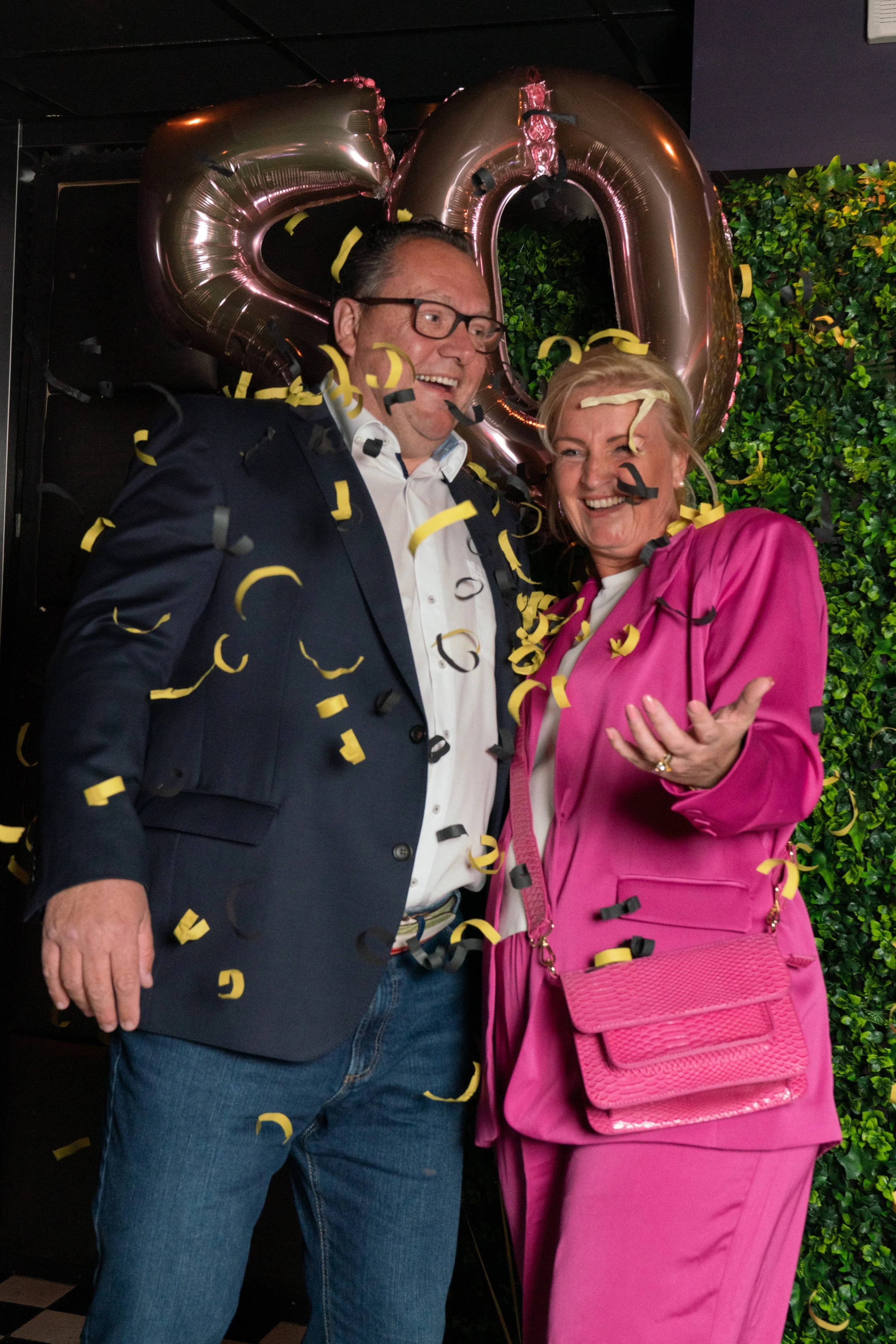 Vrolijke man en vrouw vieren feest met confetti en grote ballonnen in de vorm van de letters '50', op de achtergrond groen decor.