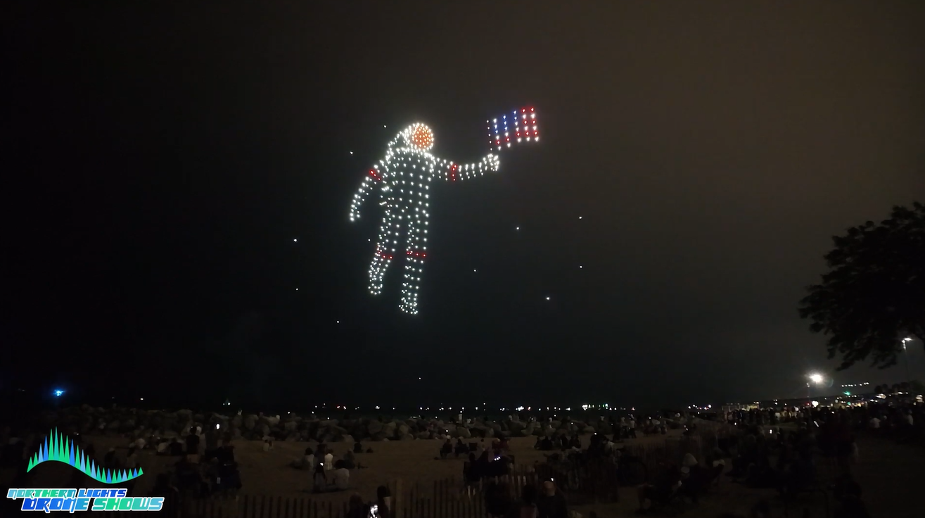 An image depicting an astronaut holding an American flag during a Northern Lights Drone Show.