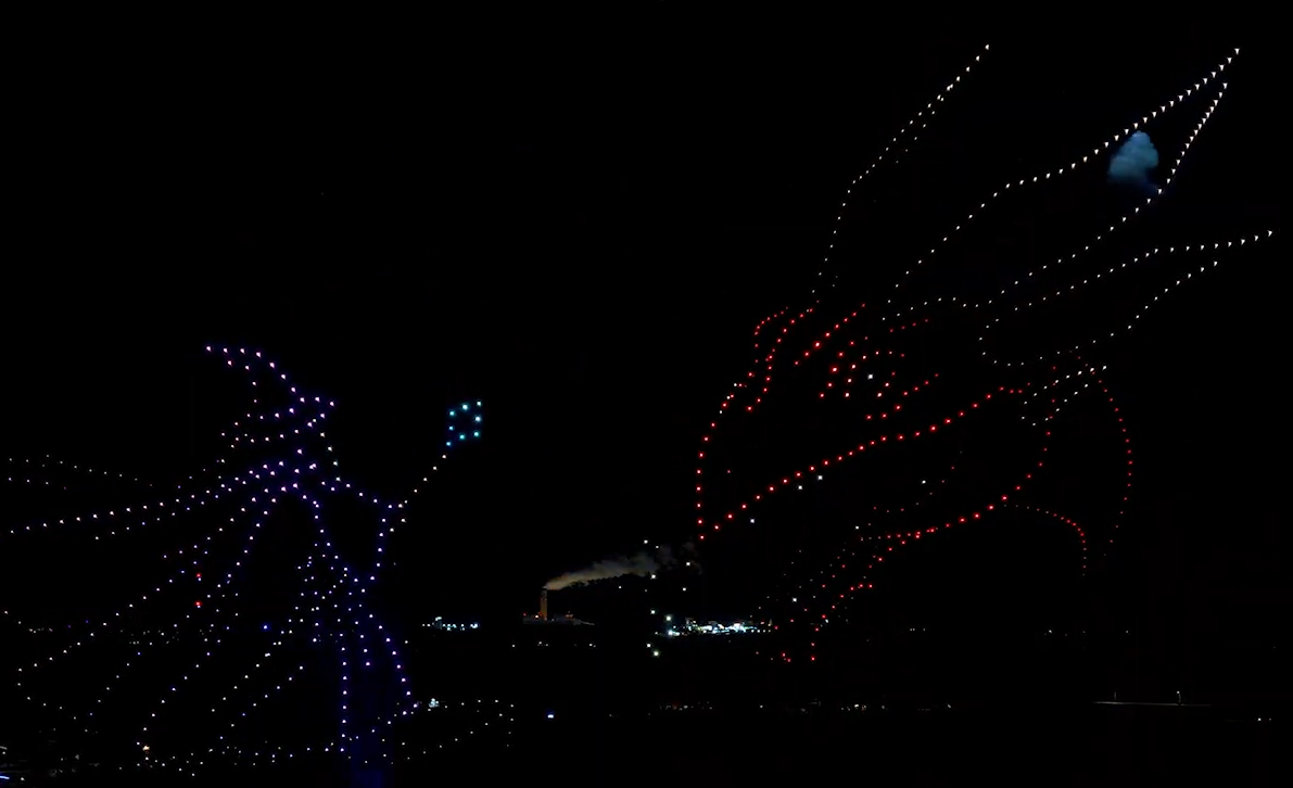 A drone show depicting a battle between a wizard and a dragon in the sky with firework-equipped drones above an audience.