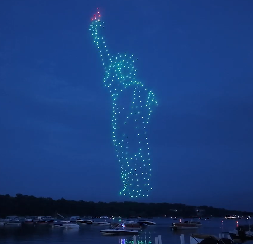 A patriotic drone show depicting the Statue of Liberty above a lake and boats for a community event.