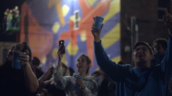 An image of a crowd of spectators cheering at an NLDS drone show above them.
