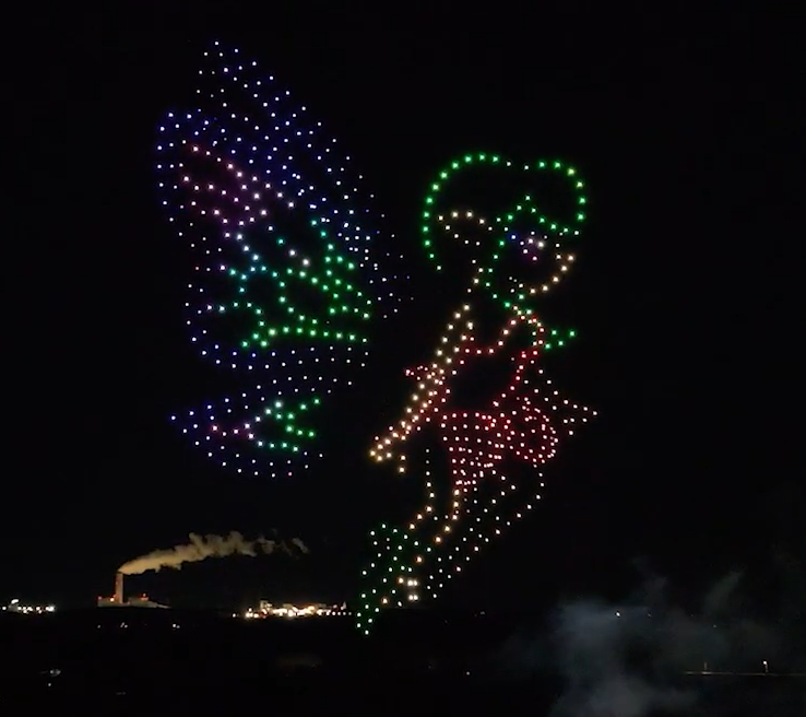 A drone show depicting a fairy with moving wings and pyrotechnics above spectators.