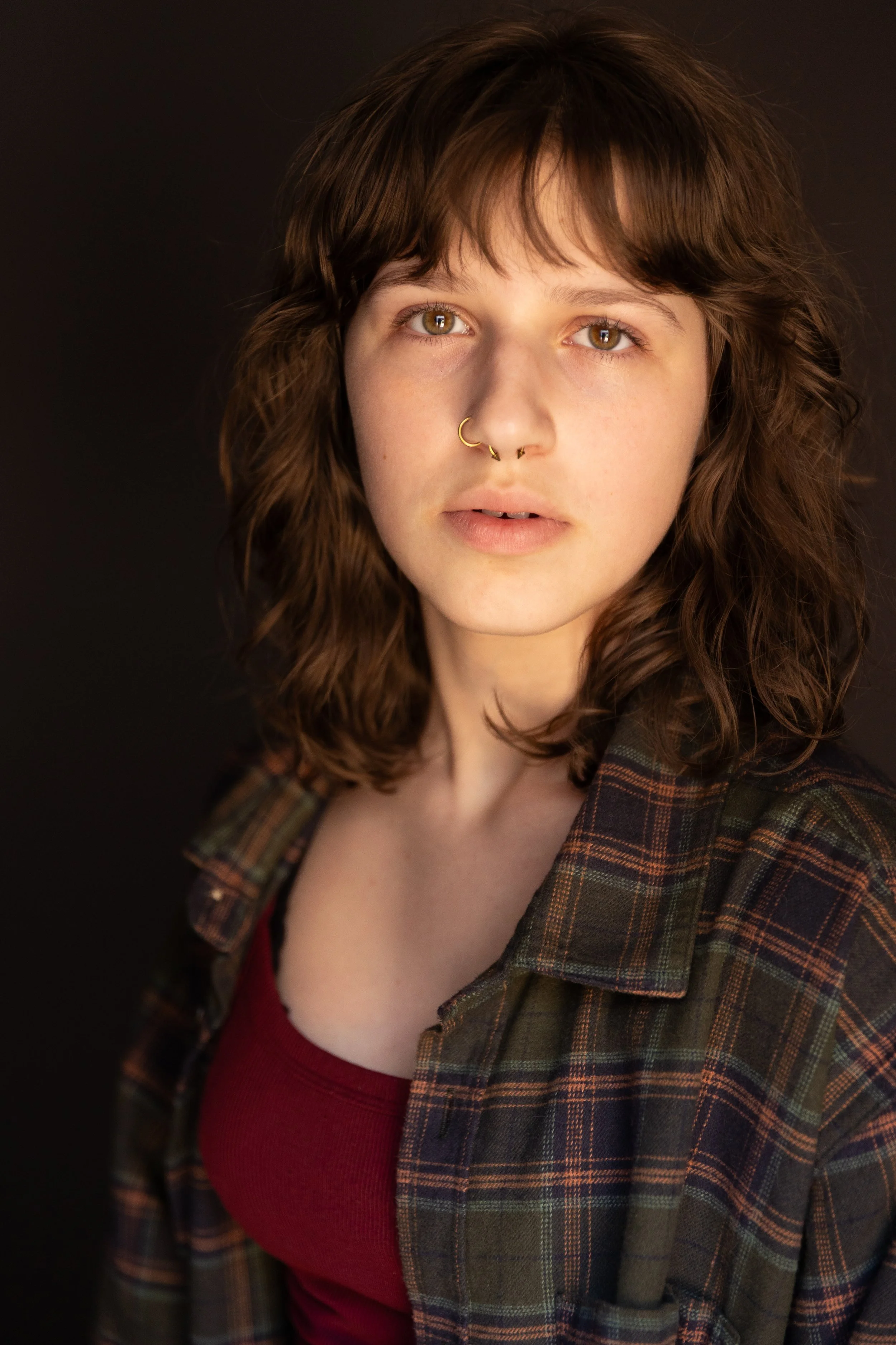 Person with long blonde hair smiling, wearing a denim jacket, standing against a brick wall.