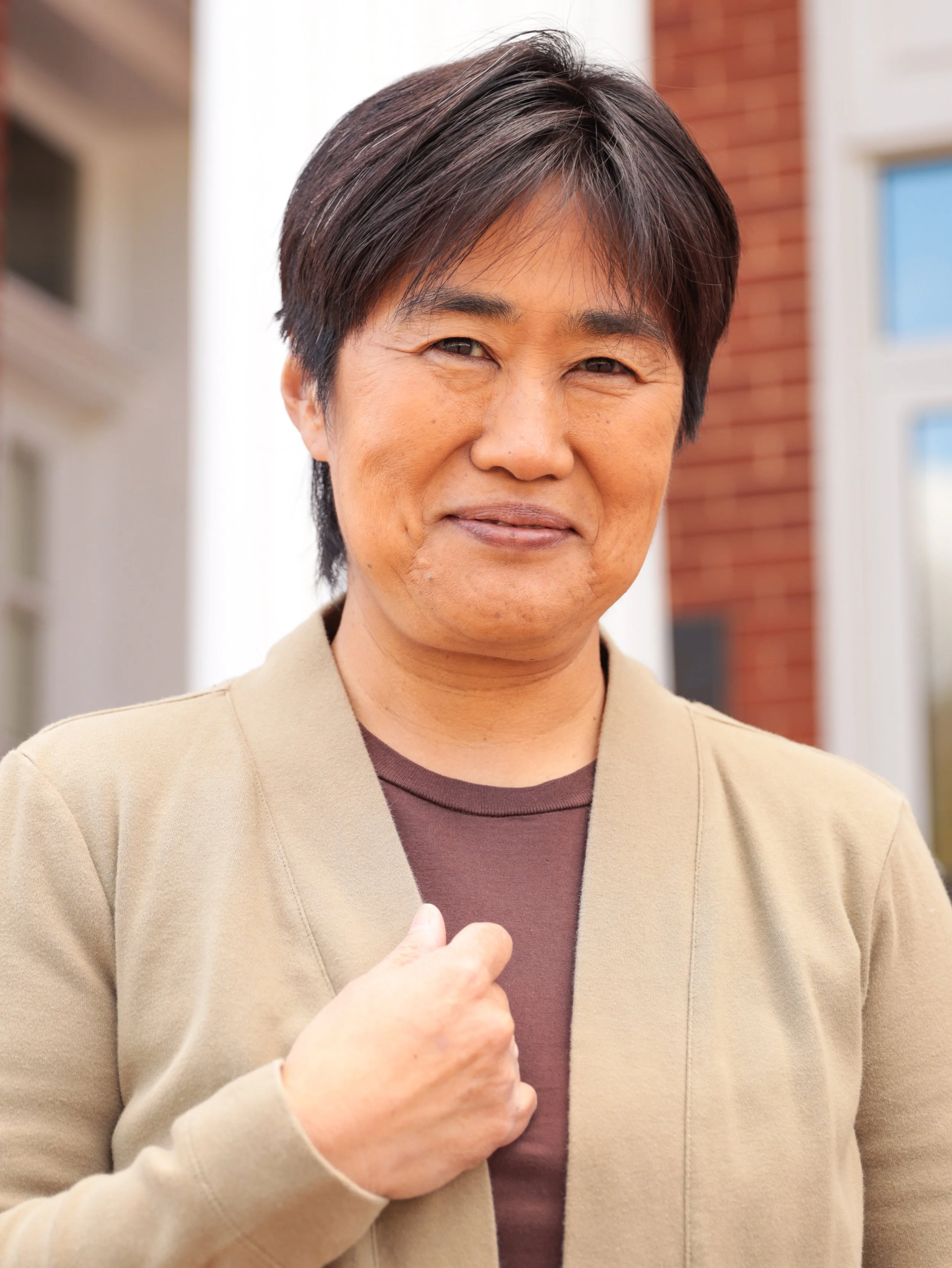 Woman in black sweater with a beaded necklace, smiling in front of a red and gray background.