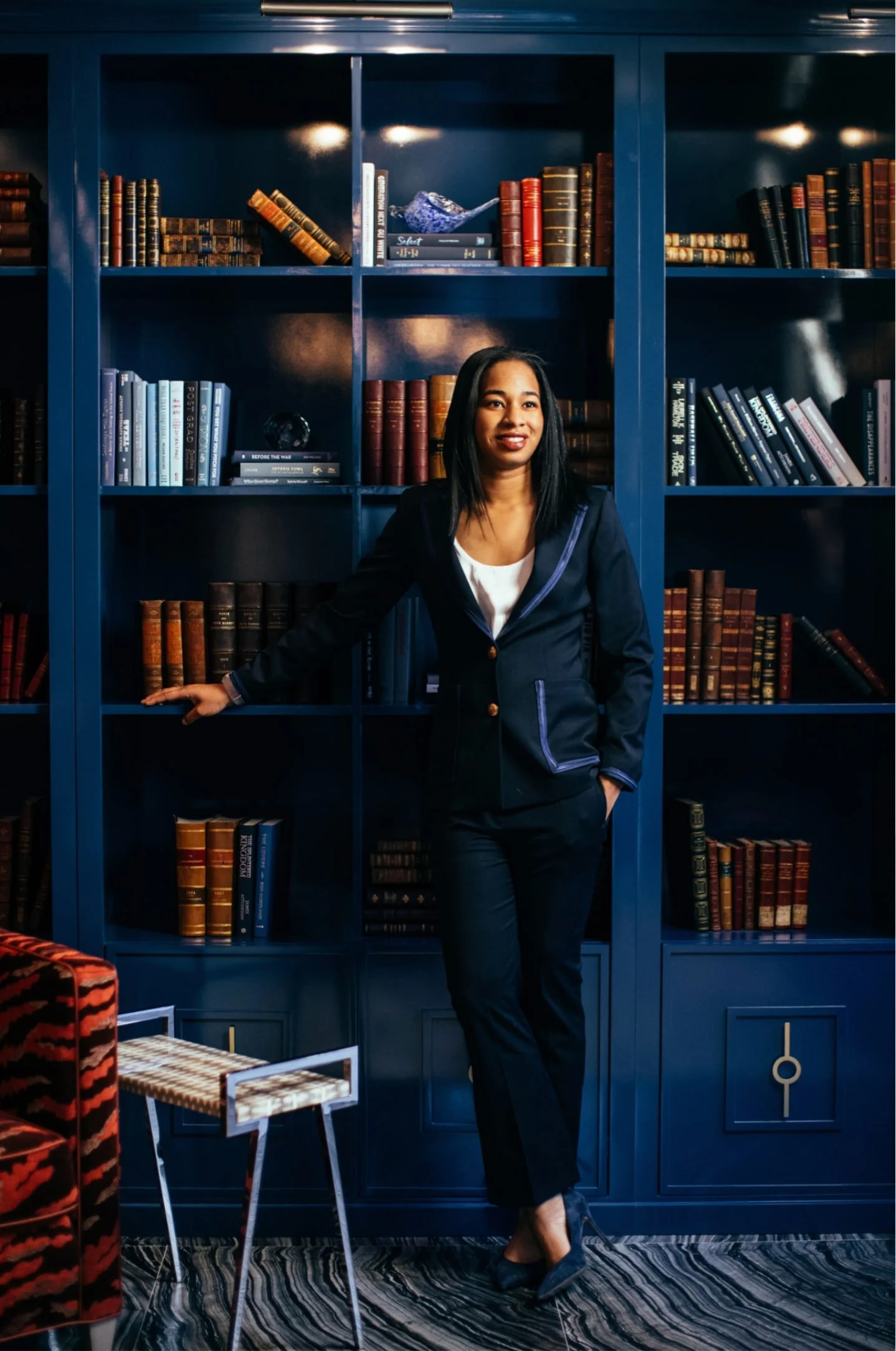 Personal branding portrait of a woman in a navy suit standing in front of blue bookshelves.