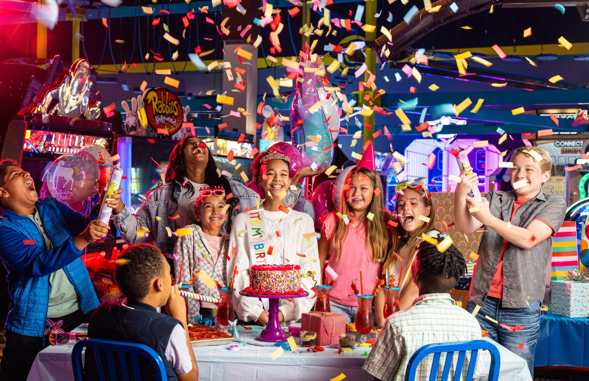 Guests celebrating around a cake as colorful confetti falls in a lively restaurant.