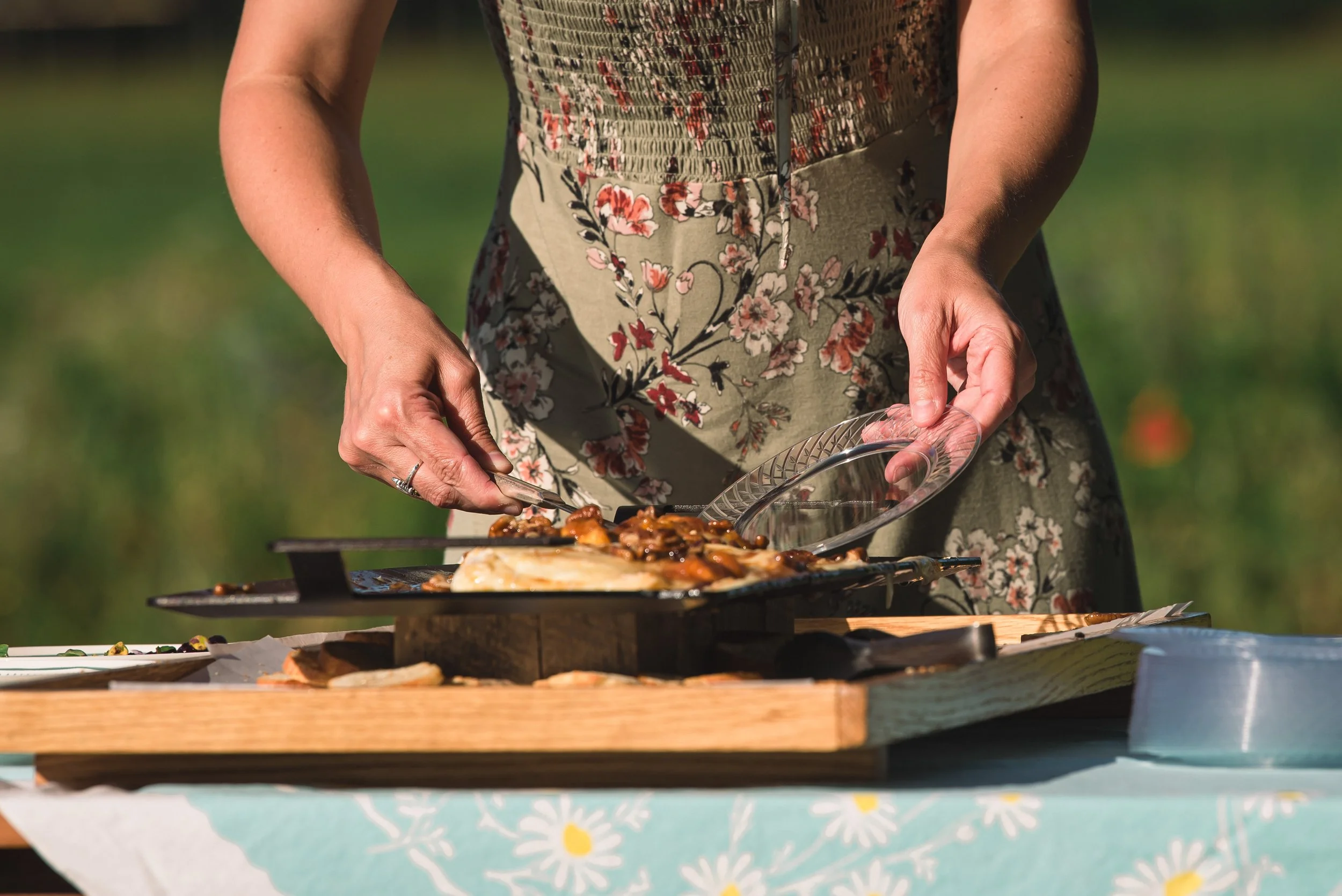 Person serving food from a platter outdoors, wearing a floral dress.