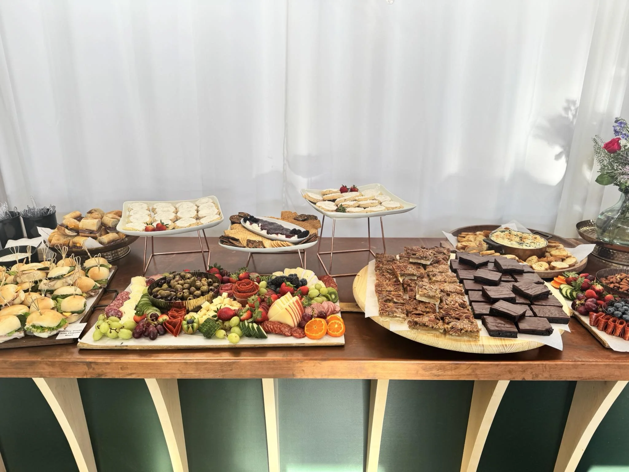 Assorted snacks including sandwiches, cheeses, fruits, chocolates, and desserts arranged on a table for a gathering or party.