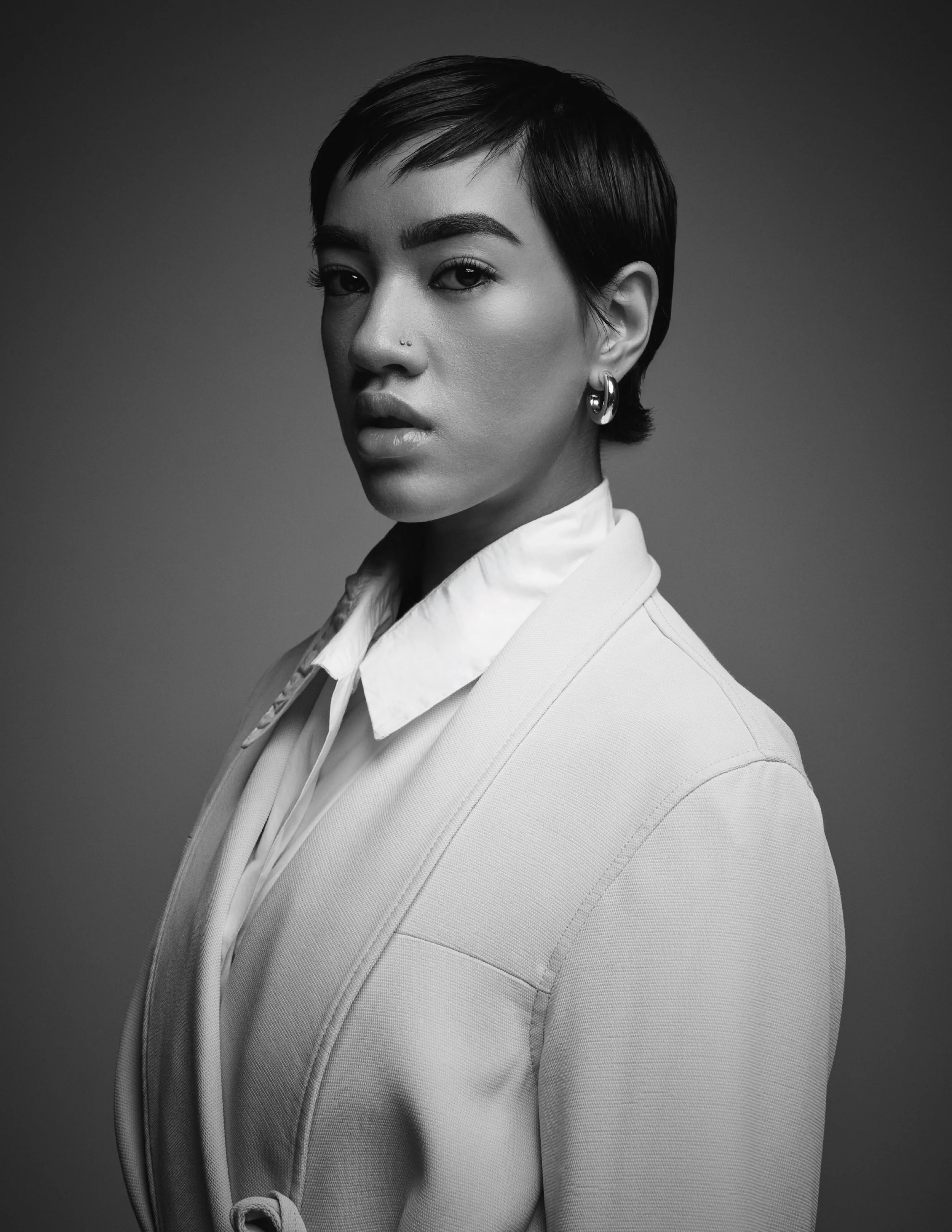 Black and white portrait of a woman with short hair, wearing a collared shirt and a blazer, looking at the camera with a serious expression.