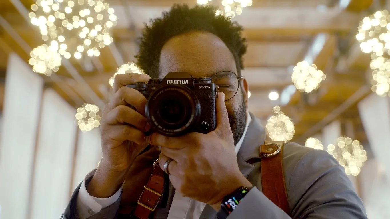 Wedding photographer using Fujifilm X-T5 camera at indoor reception venue.