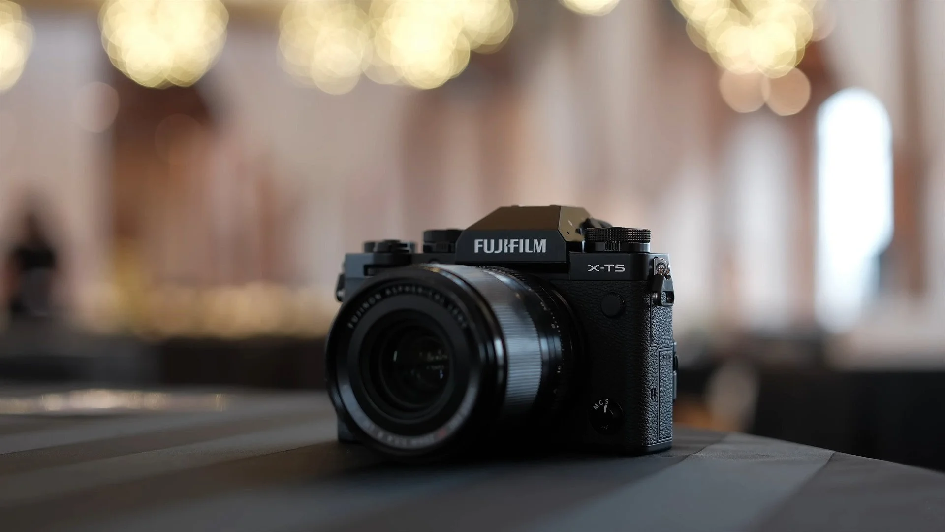 Fujifilm X-T5 camera on table inside wedding venue with lights in background.