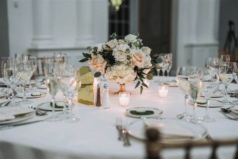 White wedding reception table with floral centerpiece and candlelight.