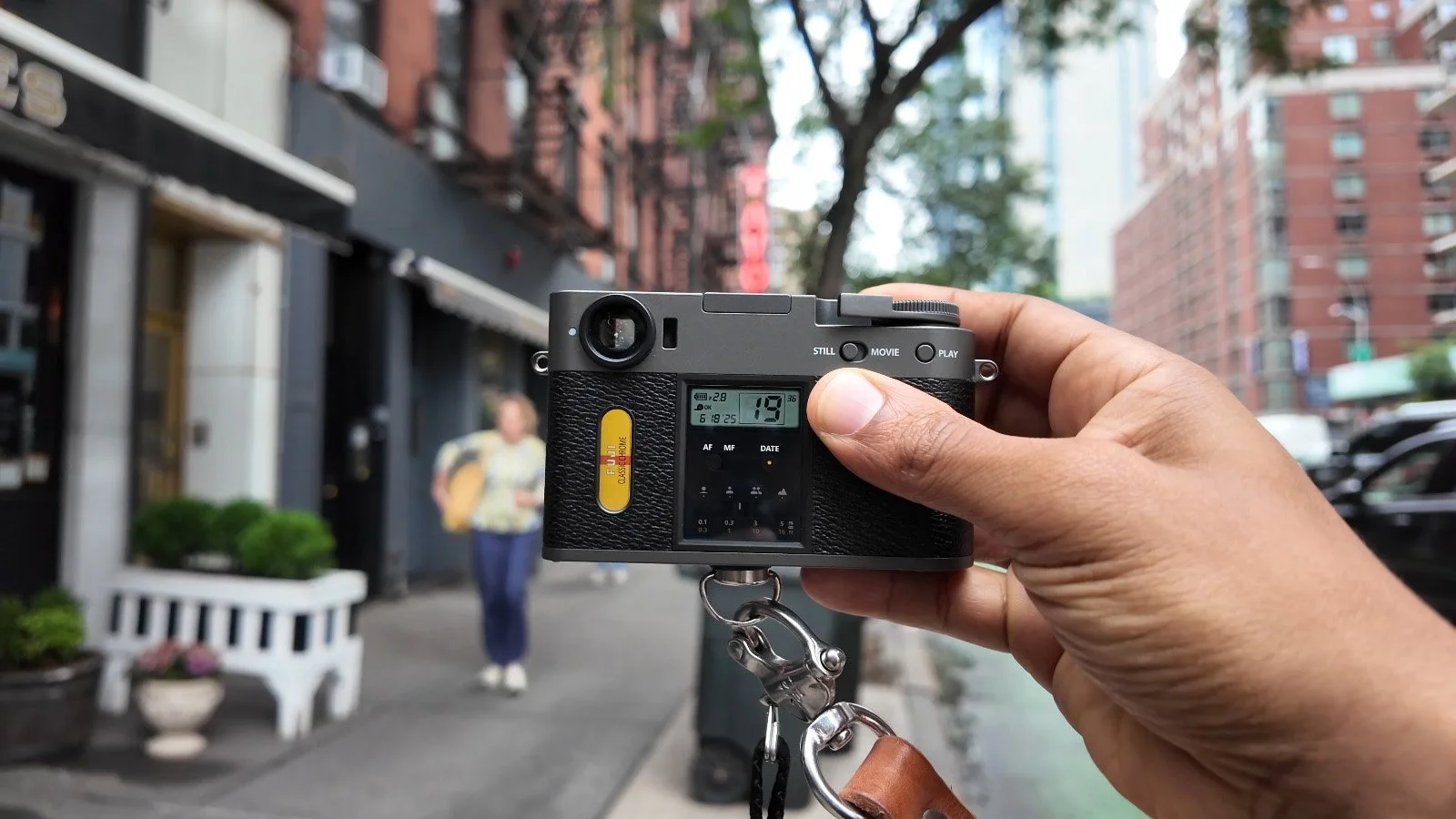 Photographer holding the Fujifilm X Half on a city street while adjusting settings.