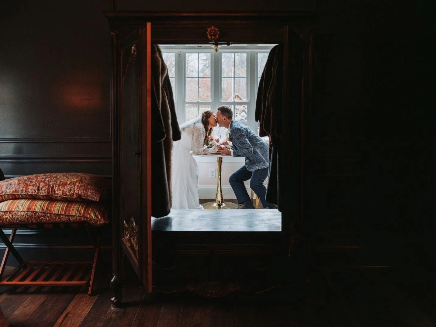 Bride and groom kissing by window framed through wardrobe.