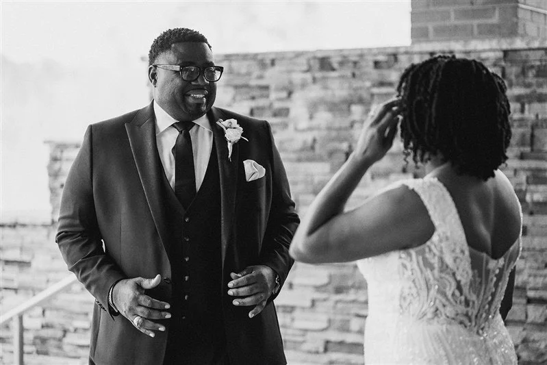 Groom smiling during first look with bride in lace wedding dress, black and white photo.