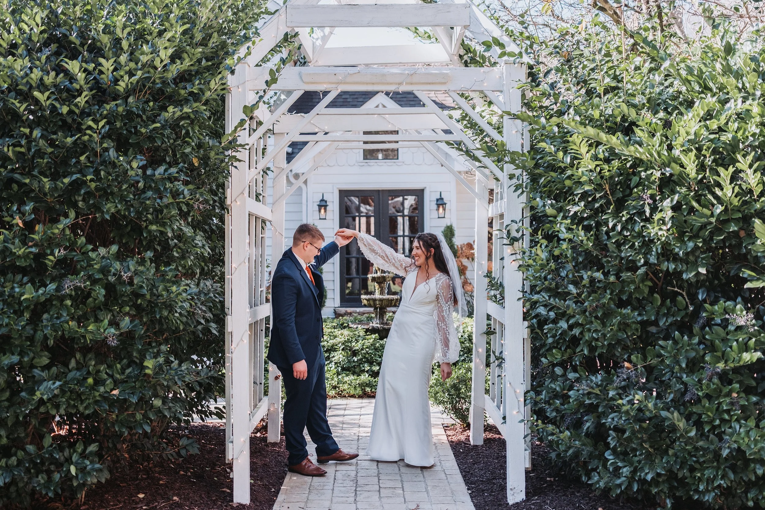 Bride and groom dancing under a white garden arbor surrounded by greenery.