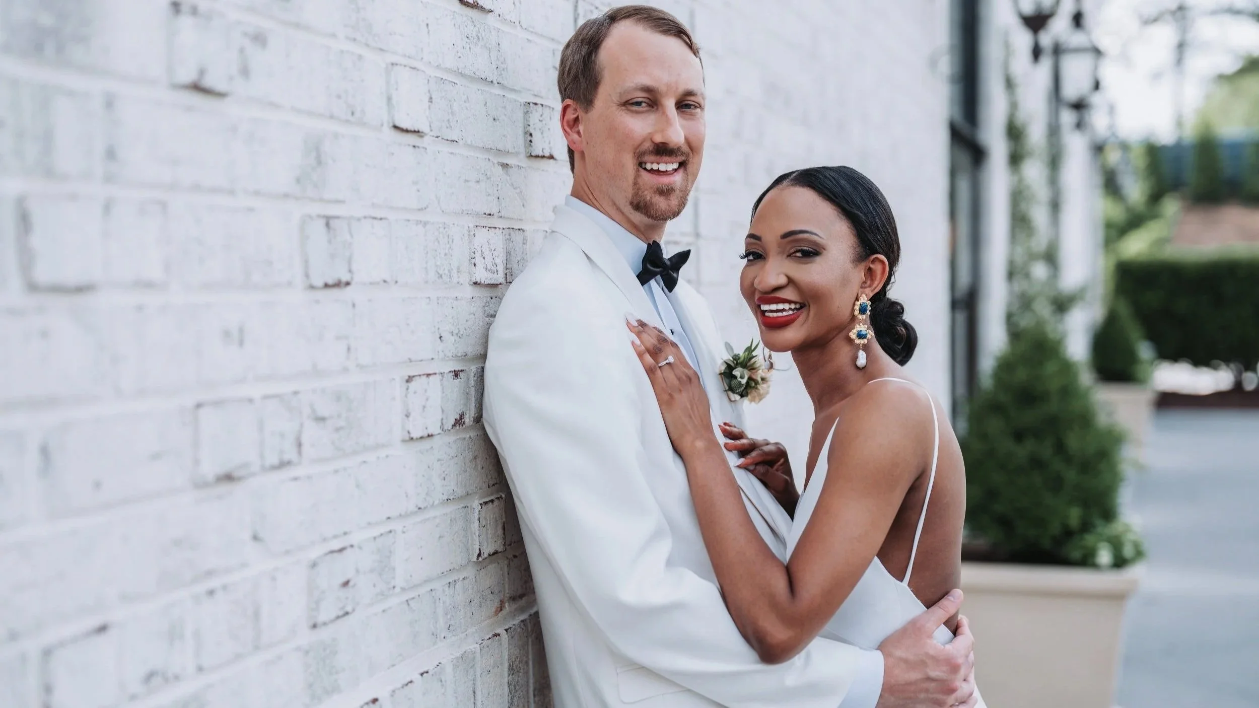 Bride and groom portrait against white brick wall at Raleigh wedding venue.
