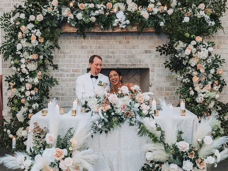 Bride and groom seated at sweetheart table with floral wedding decor.