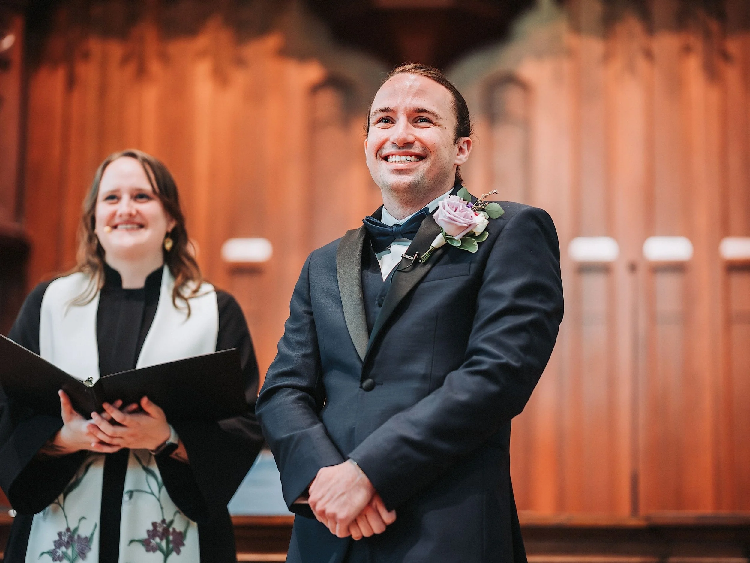 Groom smiling during a wedding ceremony in a warm indoor venue.