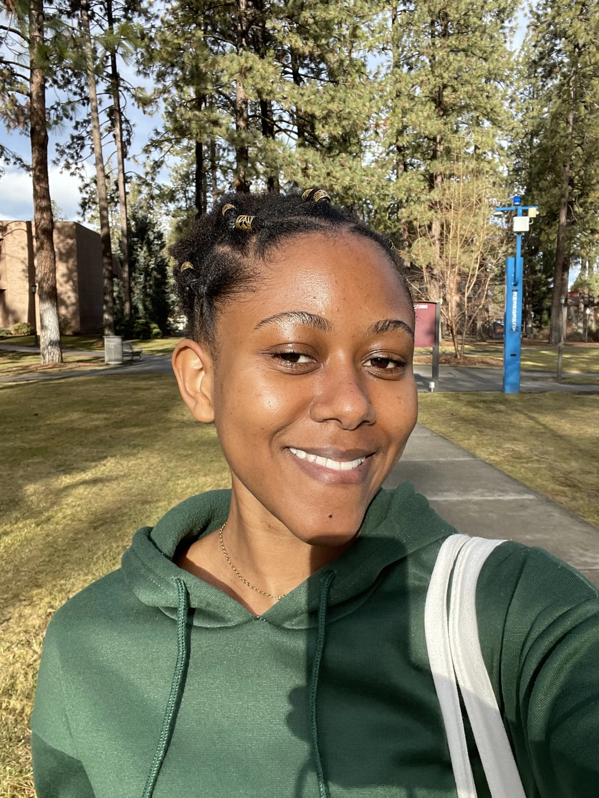 Woman smiling in green jacket with trees in background.