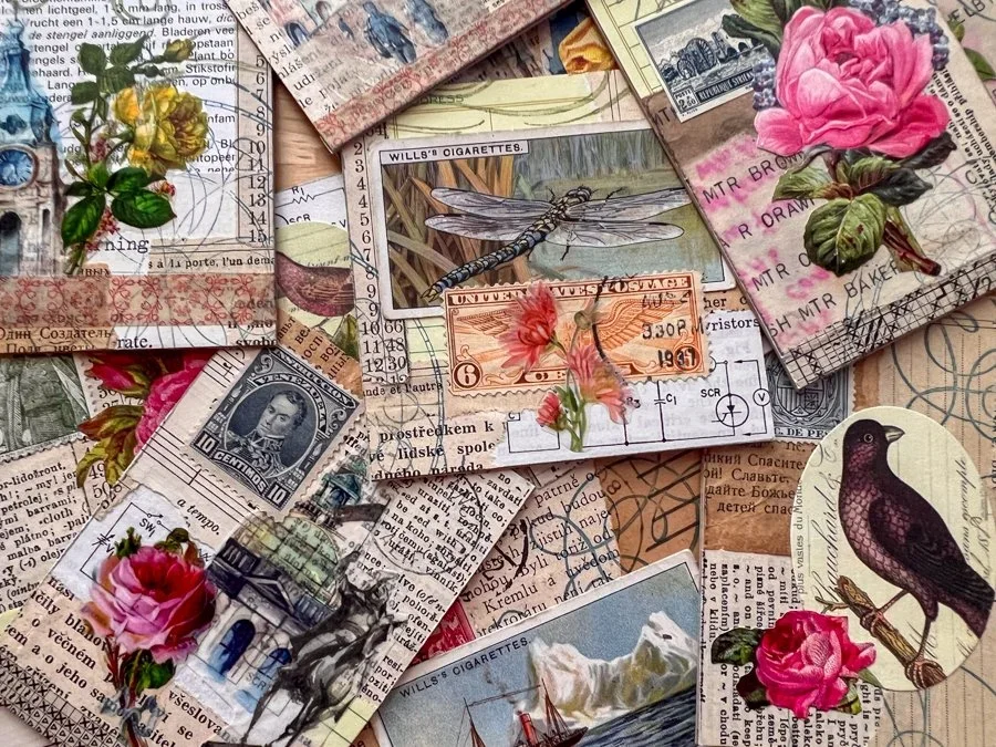A pile of ATCs (Artist Trading Cards) with vintage images of birds, dragonflies, flowers, and ocean scenes on a work table. The ATCs are stamped and display various shades of pinks, blues, greys, oranges, and natural aged paper.