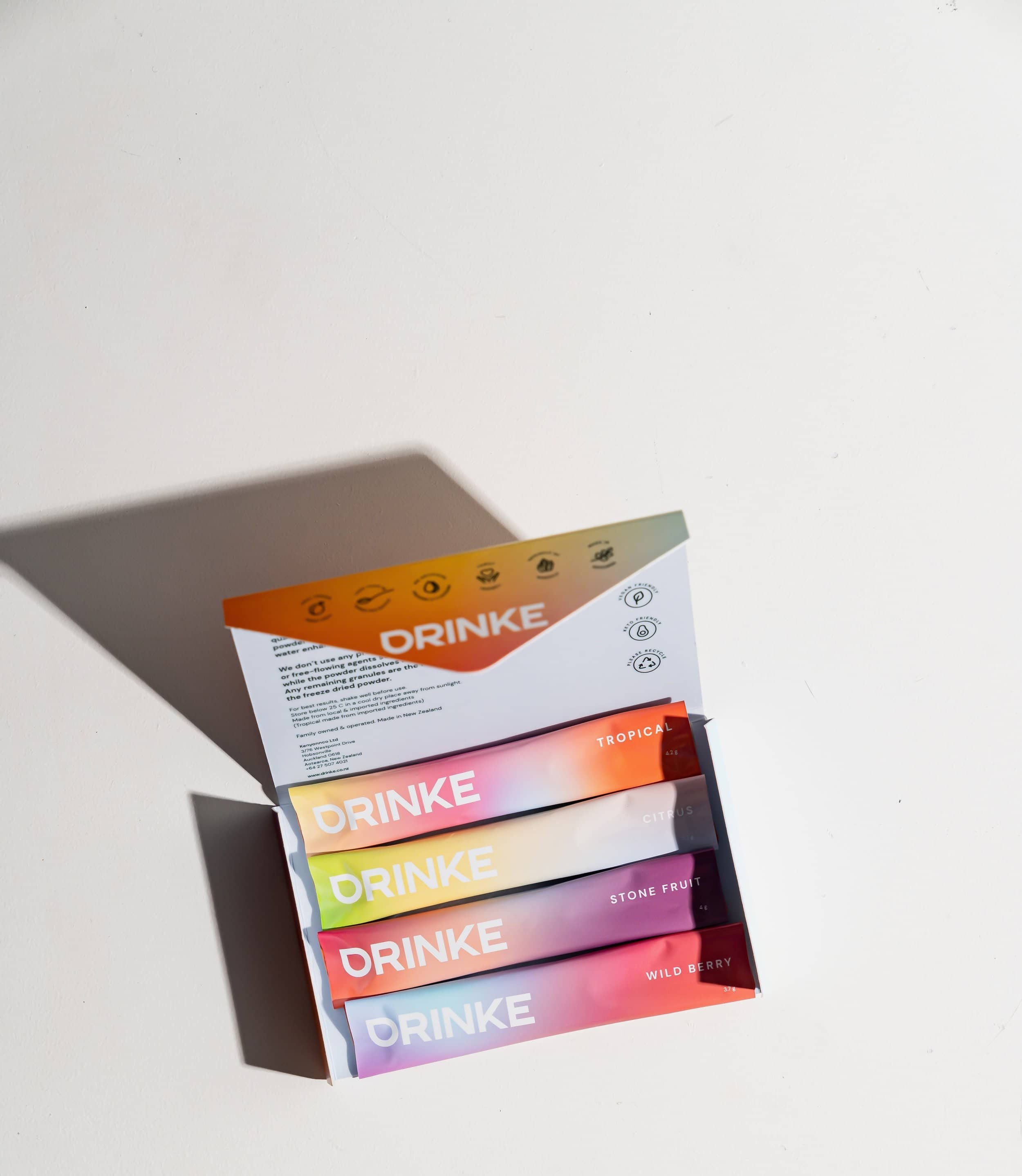 Open sample pack of DRINKE's premium water enhancers, showing four sachets in a row—Tropical, Stonefruit, Citrus, and Wildberry. Low sugar and no nasties.