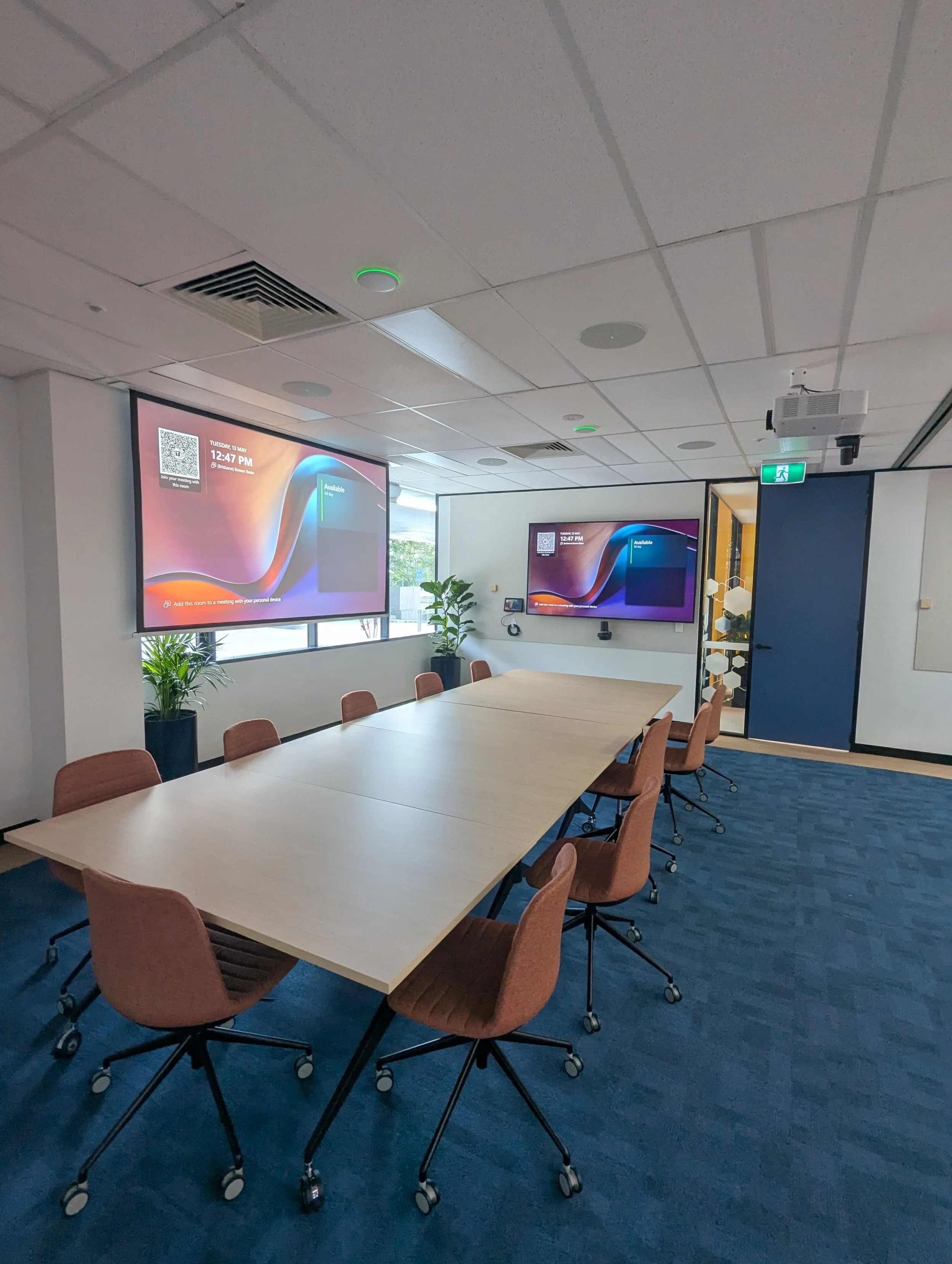 Commercial boardroom training room with projector and dual wall-mounted combinable displays and integrated video conferencing system.