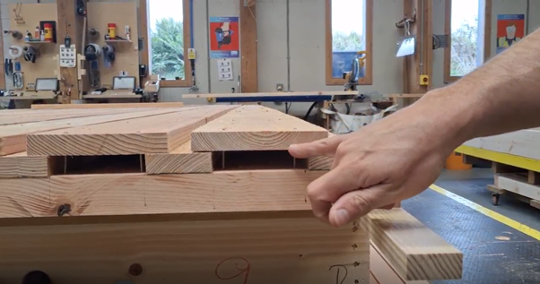 A person pointing at a stack of cut timber, part of a closed panel kit for sustainable timber homes, in MAKAR's precision manufacture workshop.
