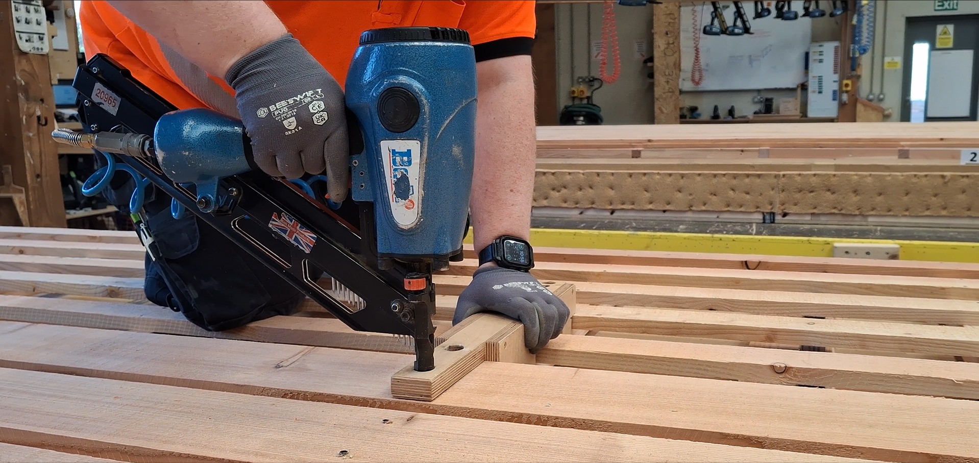 Person using a pneumatic nail gun on a piece of wood in a off-site manufacture workshop for homebuilding.