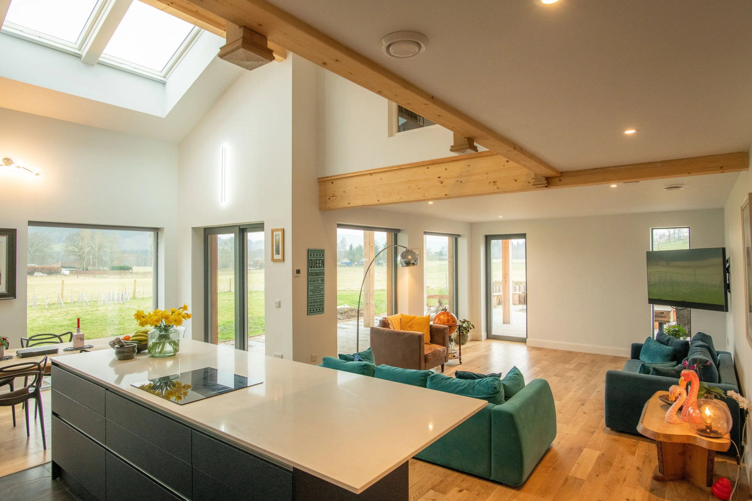 Open plan living room and kitchen in a completed MAKAR home with high ceilings, large windows, wooden beams, and outdoor views.