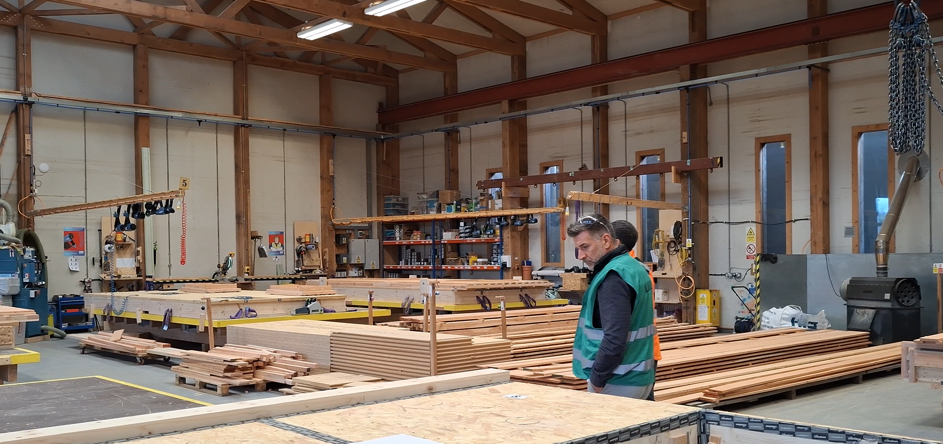 A workshop with piles of cut timber and a man in a safety vest inspecting the panels