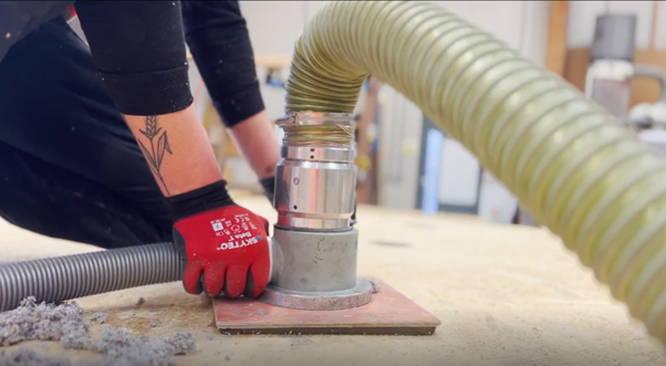 Person wearing red gloves using  tool to pump natural fibre insulation into a natural Structured Insulation Panel for sustainable homebuilding, with hoses attached.