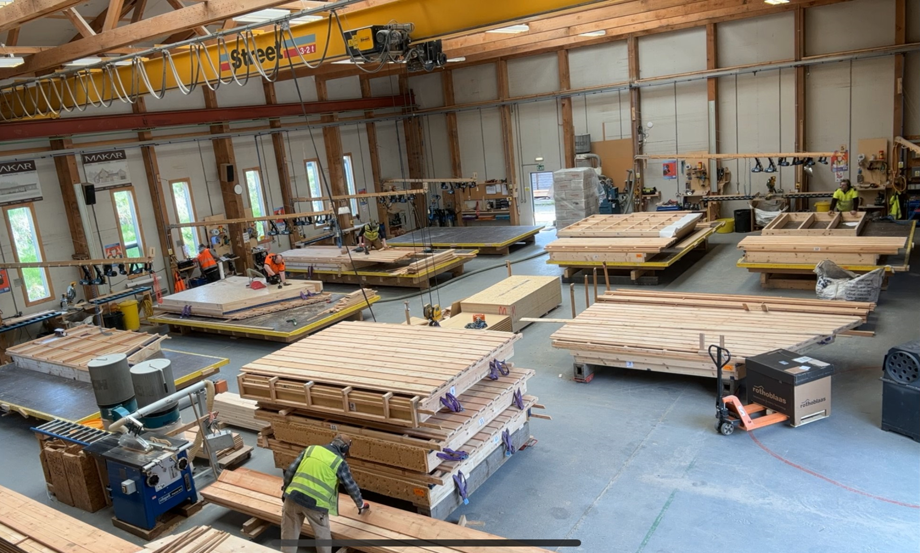 Interior of MAKAR's homebuilding workshop for precision engineering. With multiple workers, stacks of wooden planks, and various organised construction tools and equipment.