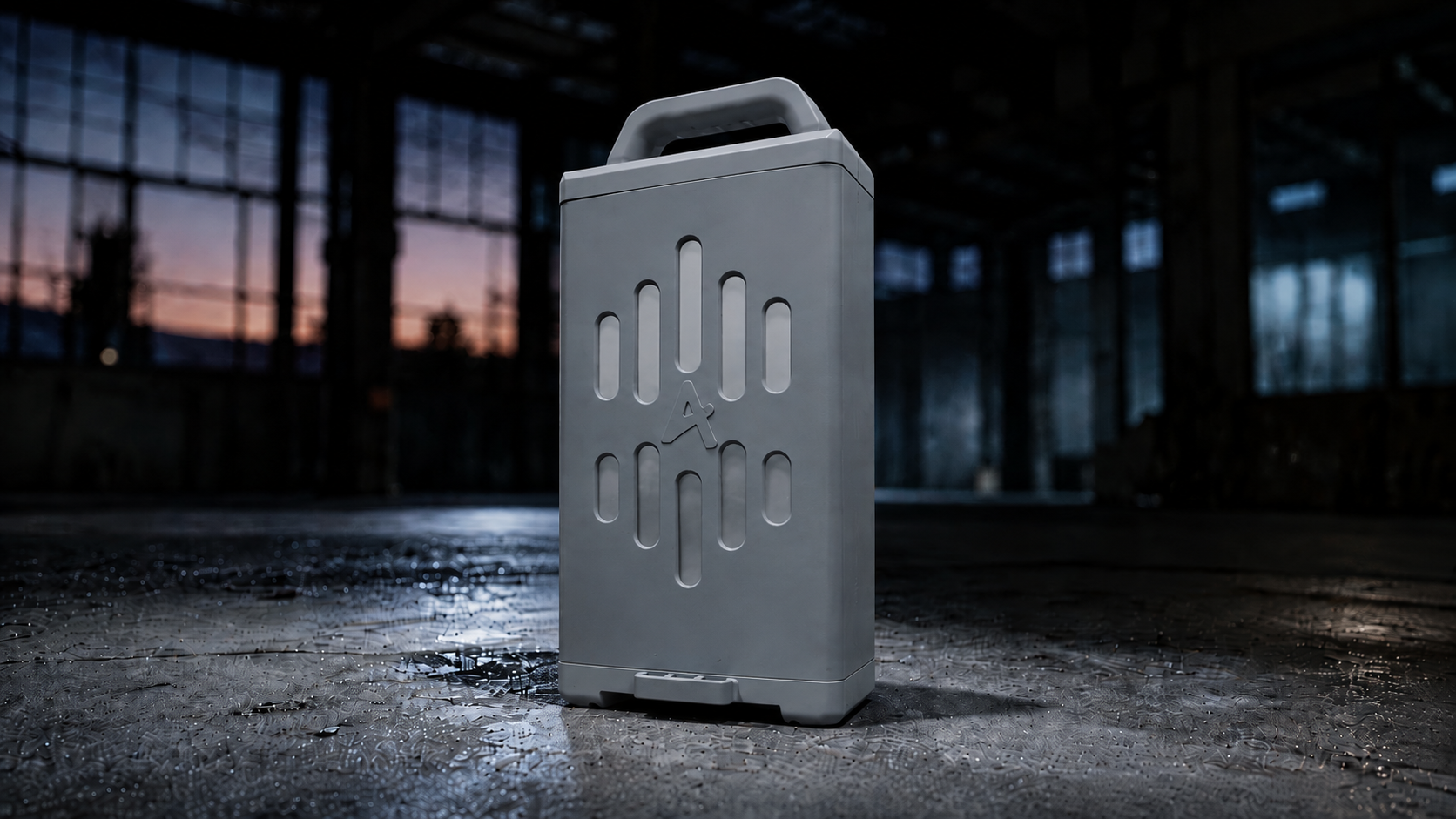 Une enceinte portable grise avec une poignée sur le dessus, placée sur une surface mouillée dans un décor industriel faiblement éclairé, avec de grandes fenêtres et un ciel de couchant visible à l'extérieur.