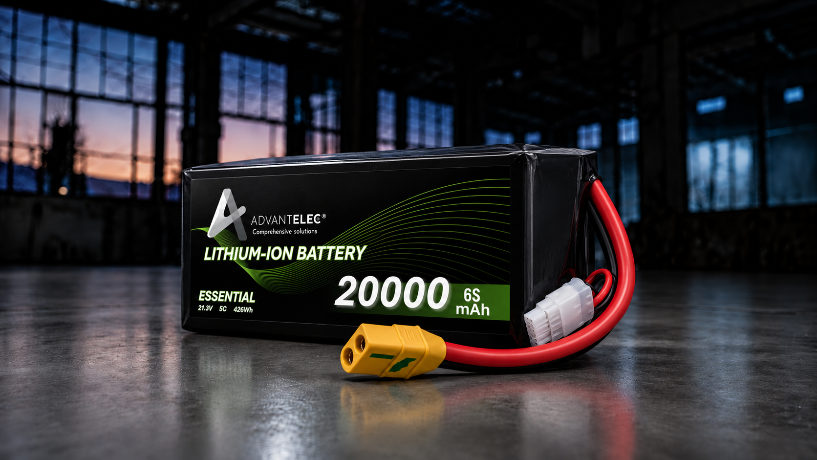 Une batterie lithium-ion noire avec des câbles rouges et jaunes, placée sur une surface réfléchissante dans un entrepôt ou un bâtiment industriel doté de grandes fenêtres révélant un ciel de coucher de soleil en arrière-plan.