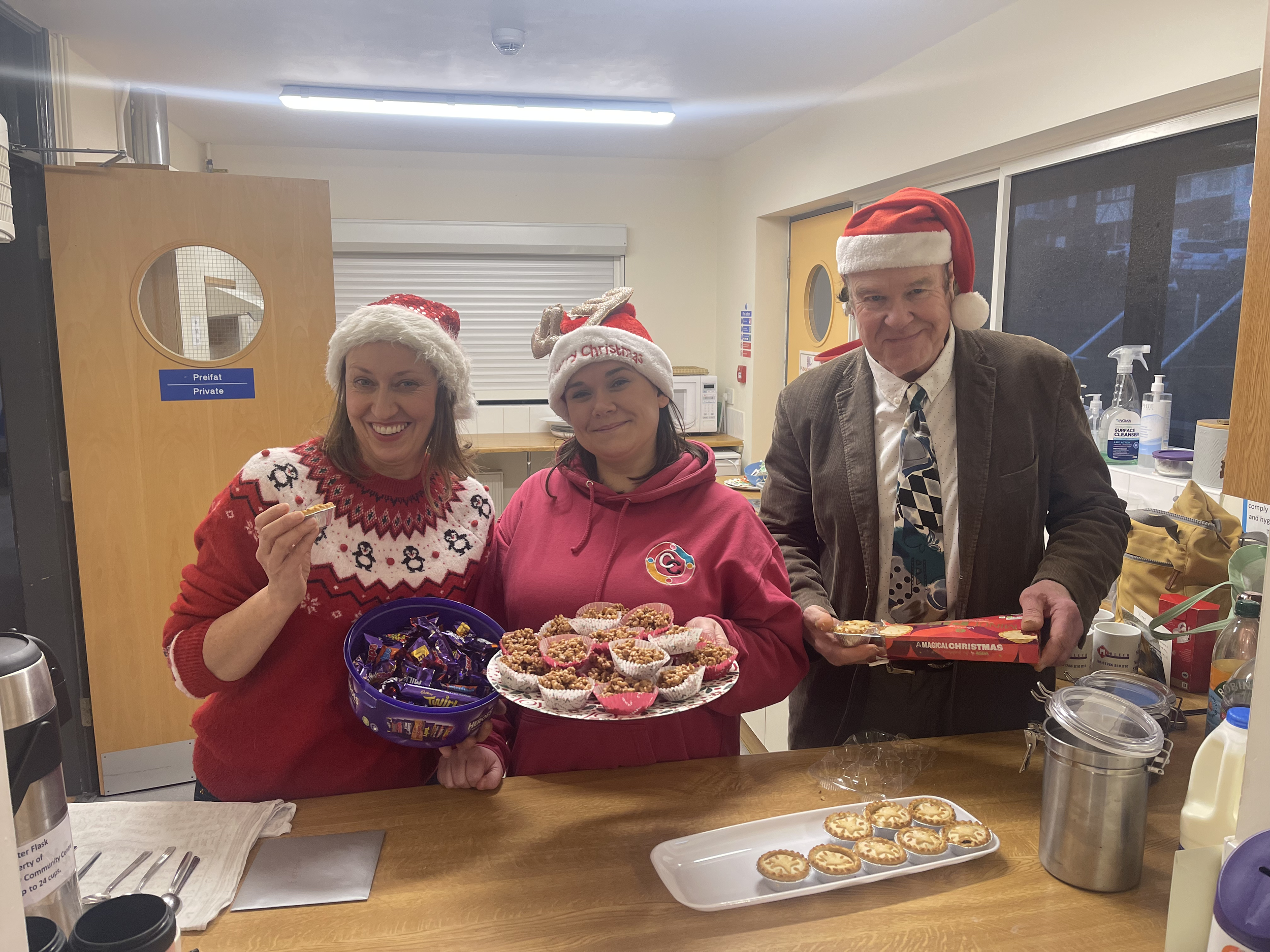 Arweinwyr y grŵp Eva a Lydia gyda'r gwirfoddolwr Chris yn arddangos y nwyddau Nadolig.