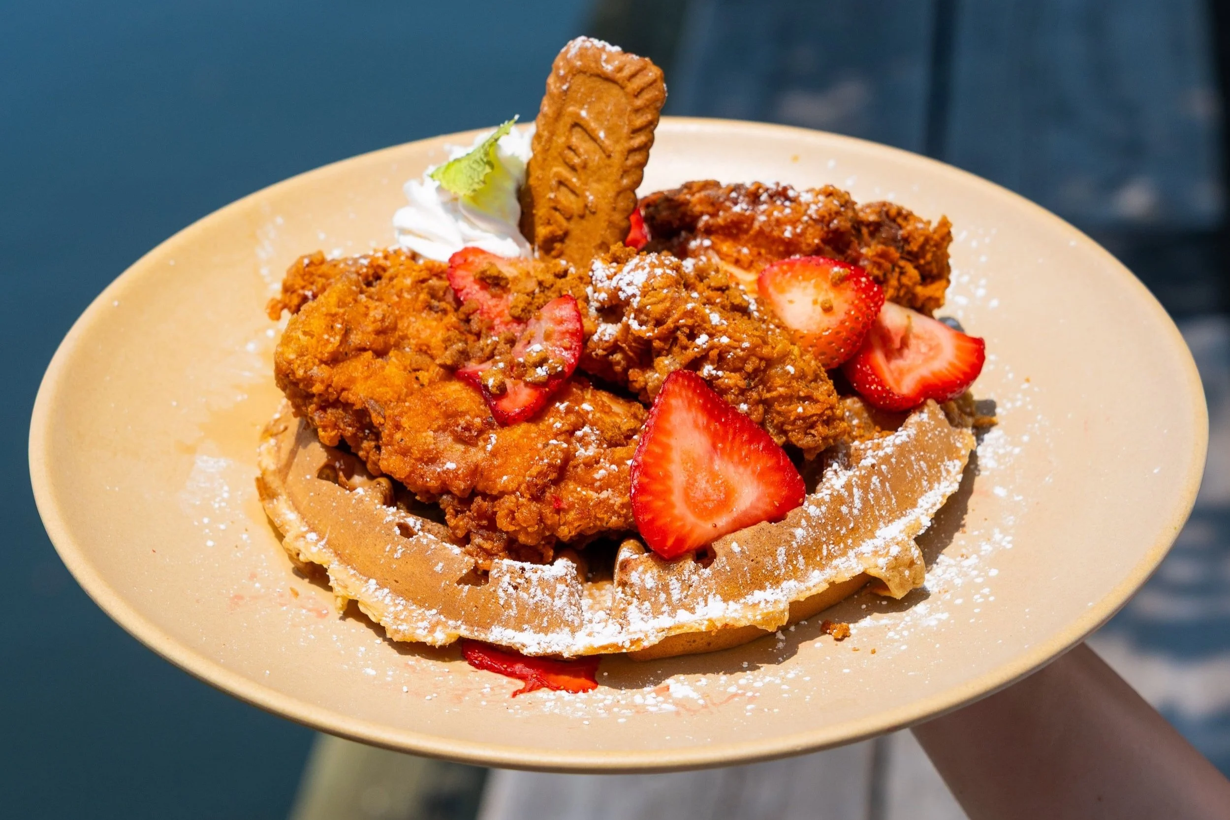 Southern-style chicken and waffles topped with fresh strawberries, powdered sugar, and a cookie garnish.