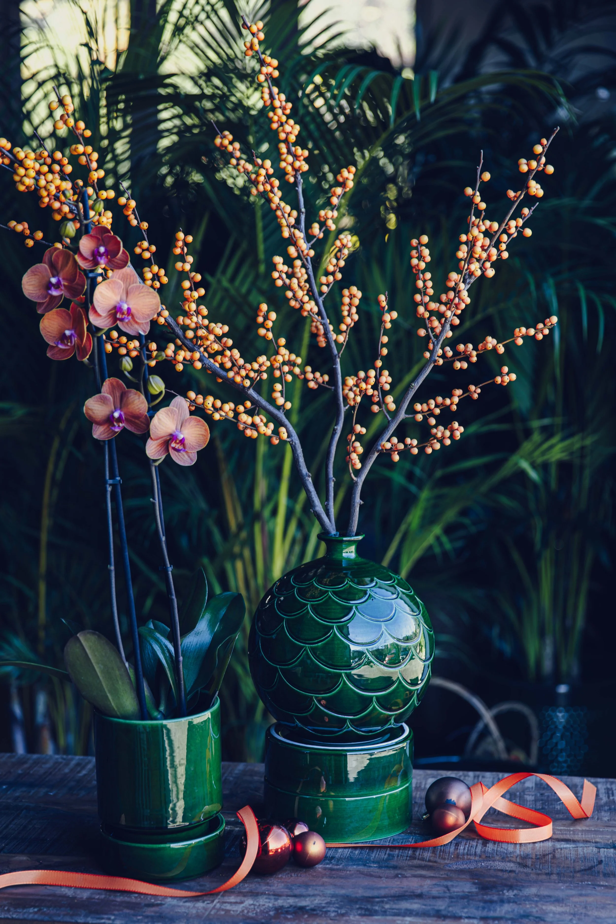 Pink orchids and orange berry branches in green glazed ceramic vases, festive floral arrangement for Christmas