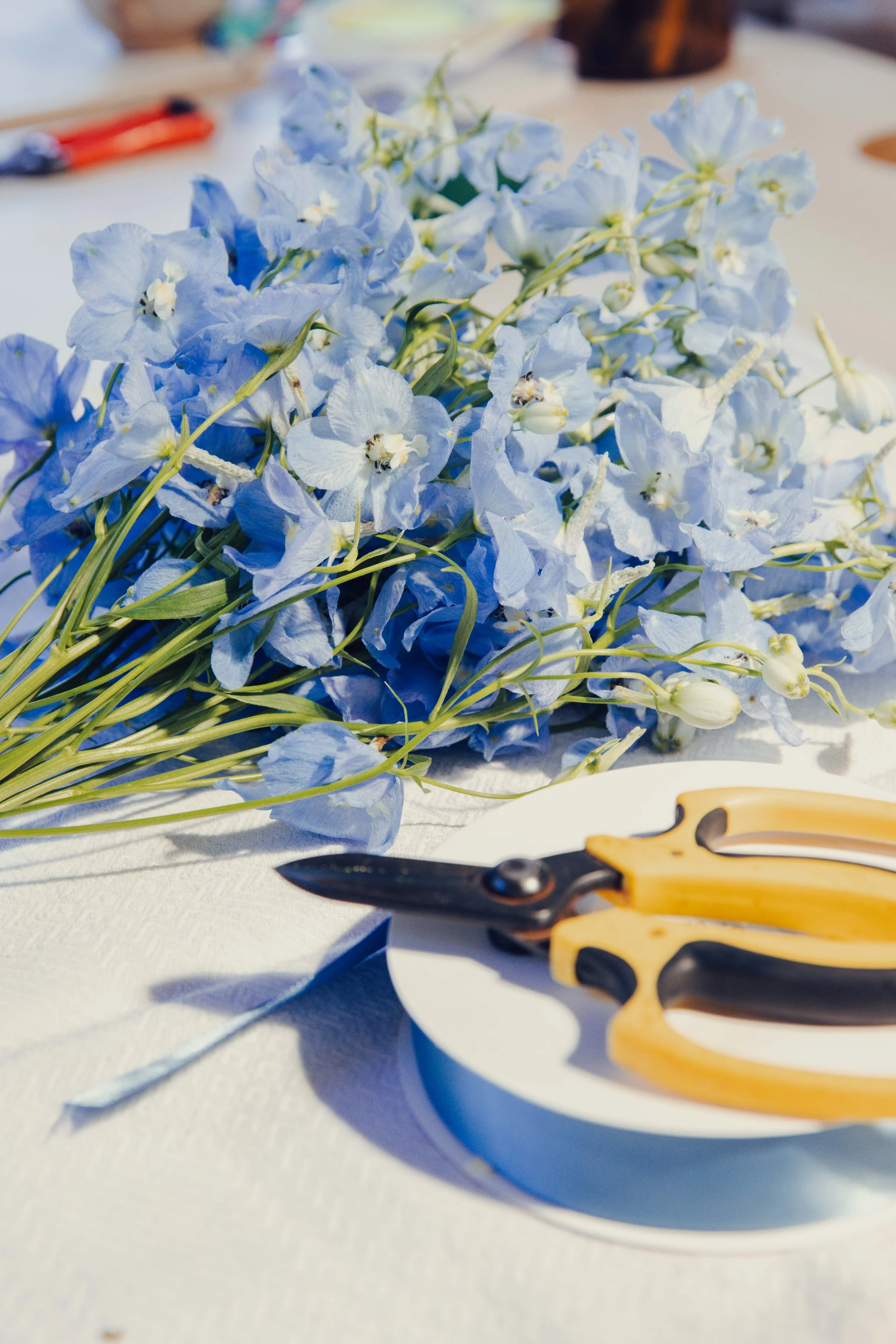 Blue delphinium stems and yellow florist secateurs on a white work surface, event flowers prepared in the GRÖNT studio