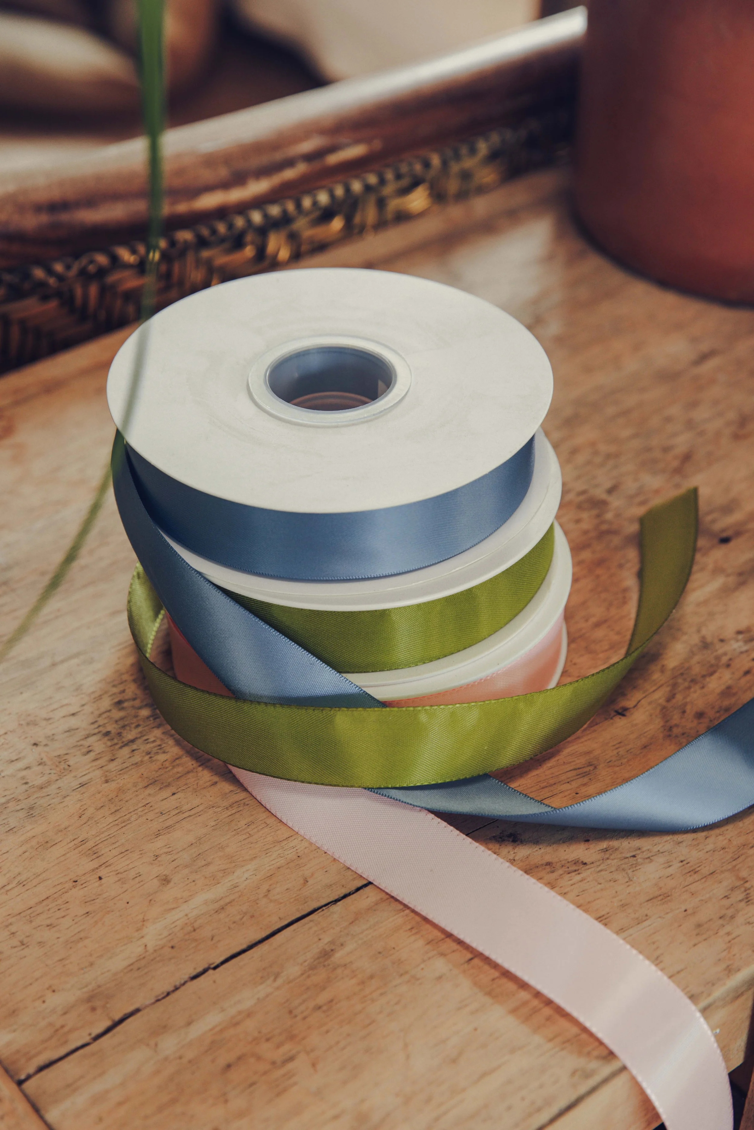 Rolls of blue, olive green and blush satin ribbon on a wooden table, florist materials for event flowers