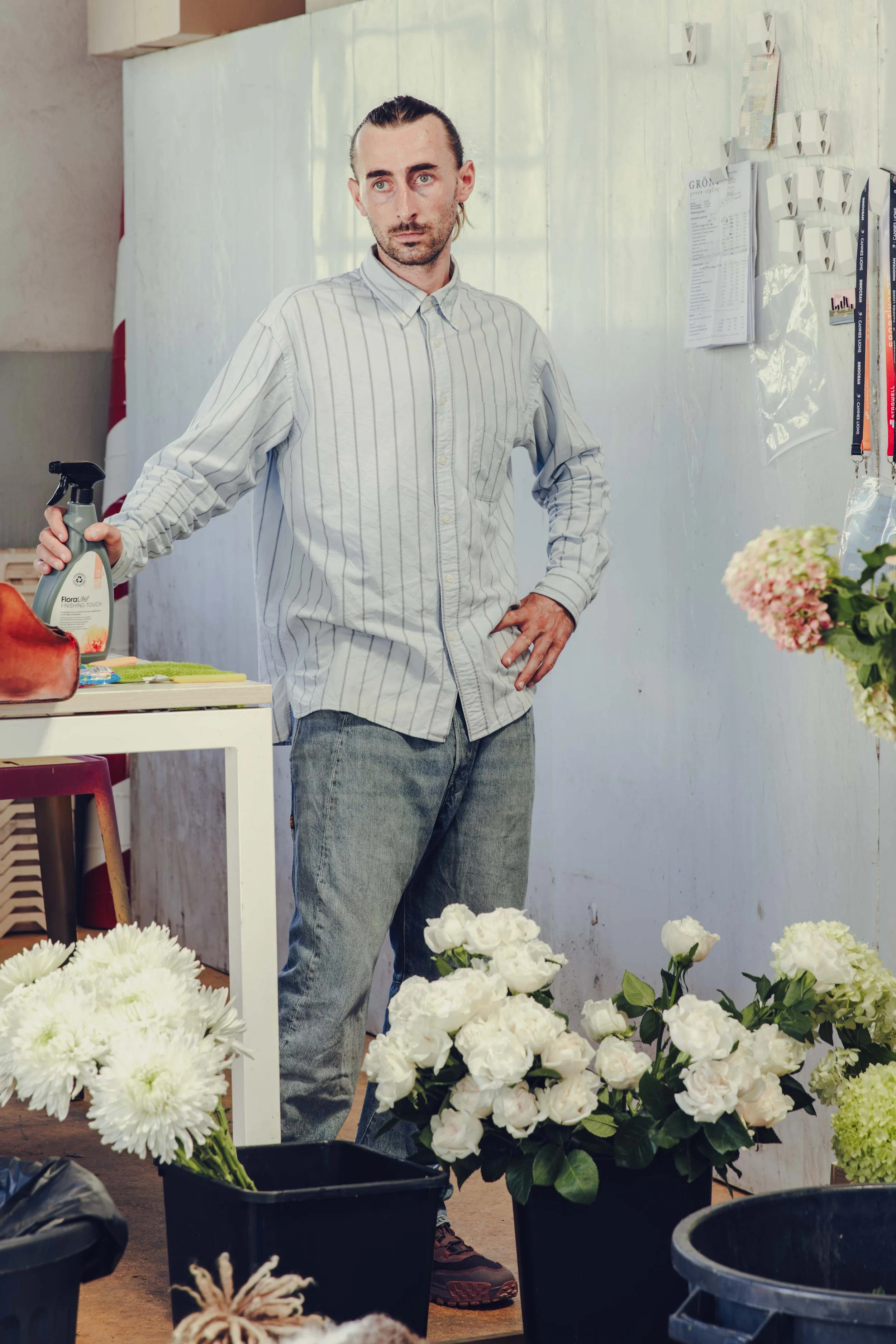 Florist standing in the studio beside buckets of white roses and hydrangea