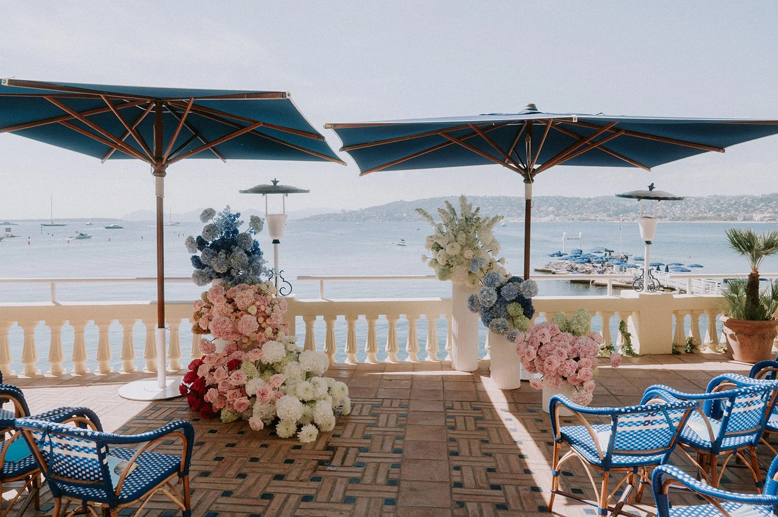 Antibes wedding terrace with blue umbrellas, rattan chairs and cascading blue, pink and white flower installations