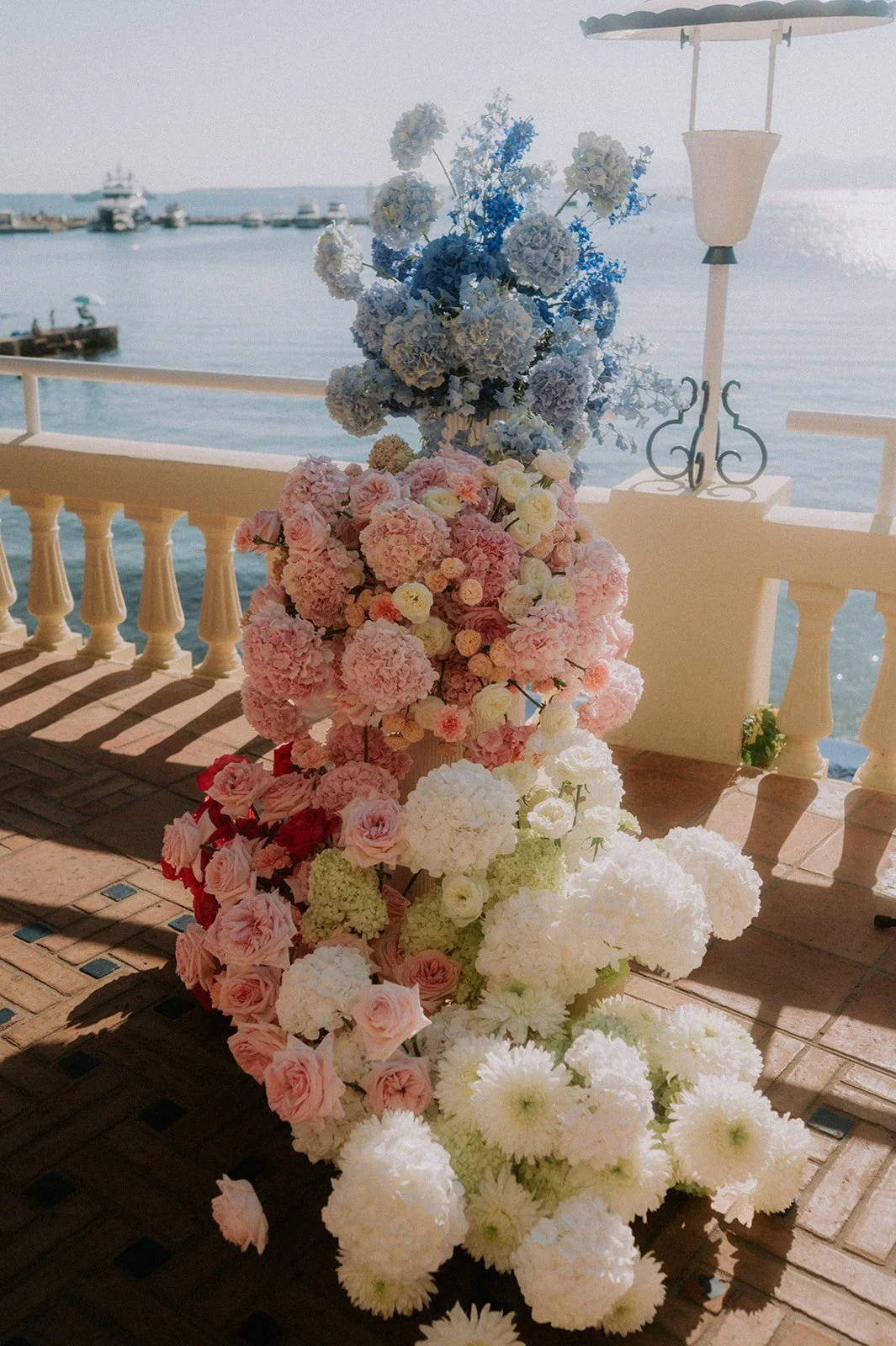 Cascading wedding flower installation of blue hydrangea, pink garden roses and white chrysanthemum above the sea, Antibes