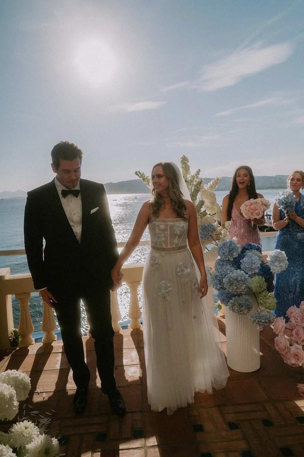 Bride and groom walking down the aisle past hydrangea and white flower installations at a seaside wedding ceremony, French Riviera