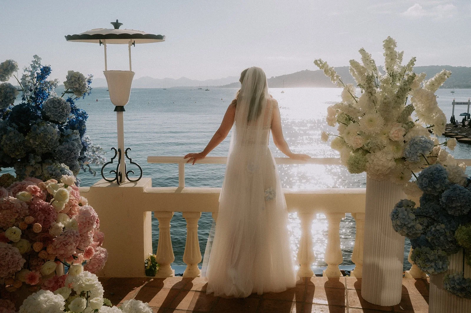 Bride at a sea-view terrace balustrade between tall white delphinium and blue hydrangea wedding arrangements, Antibes